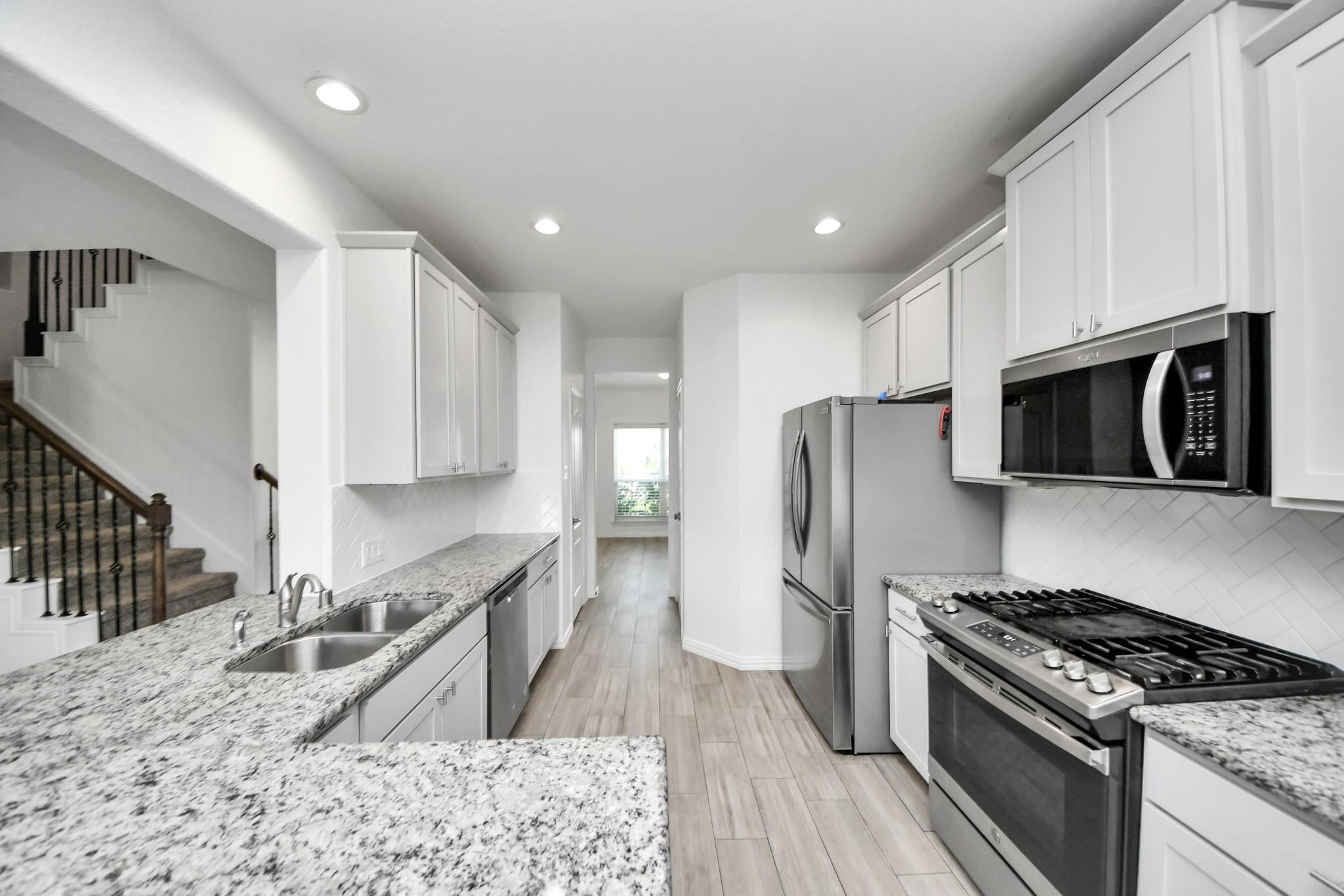 Kitchen with white cabinets, speckled granite counters, stainless appliances, and a staircase alongside.