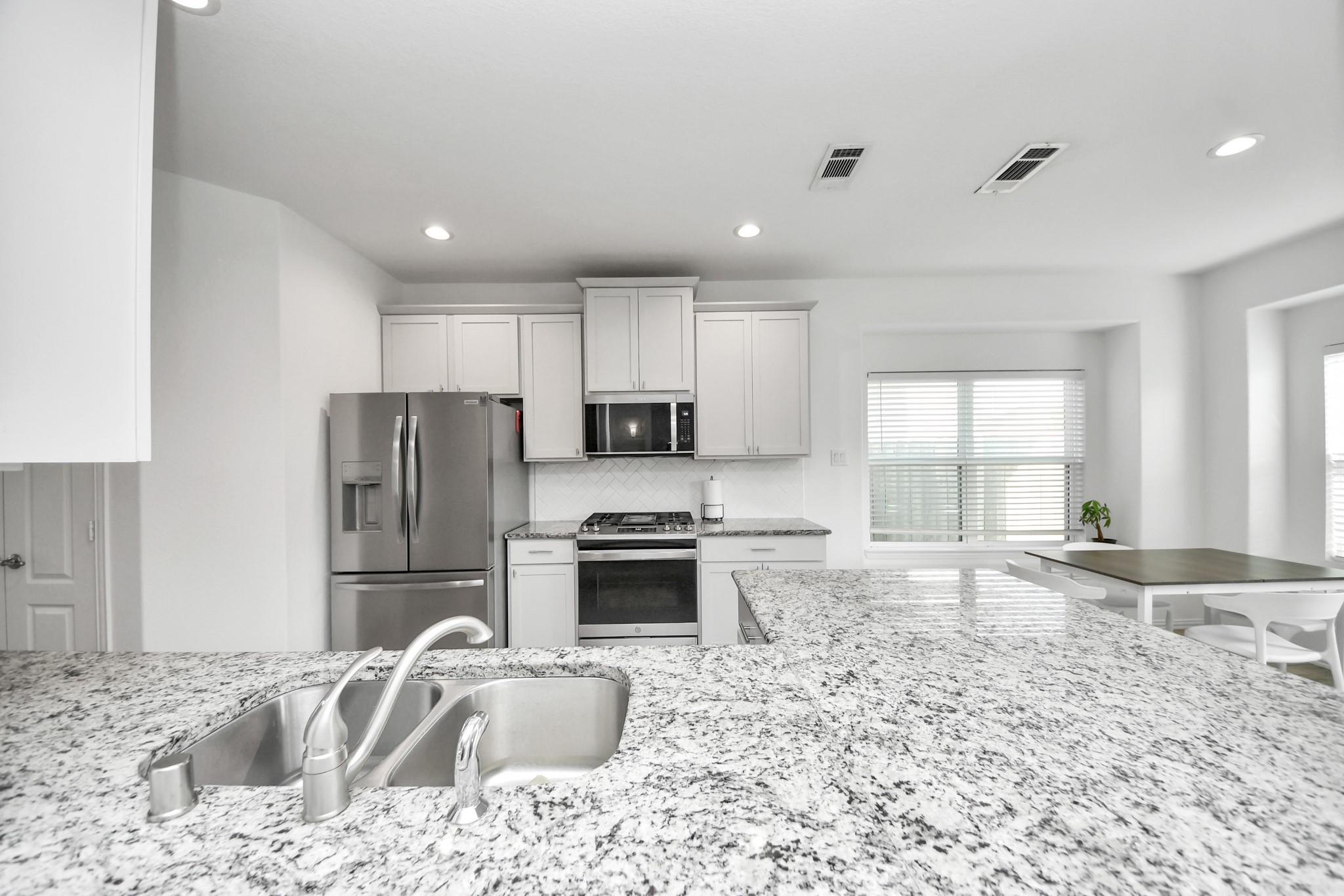 Kitchen with a granite island and sink, white cabinetry, stainless steel appliances, and an adjoining dining area.