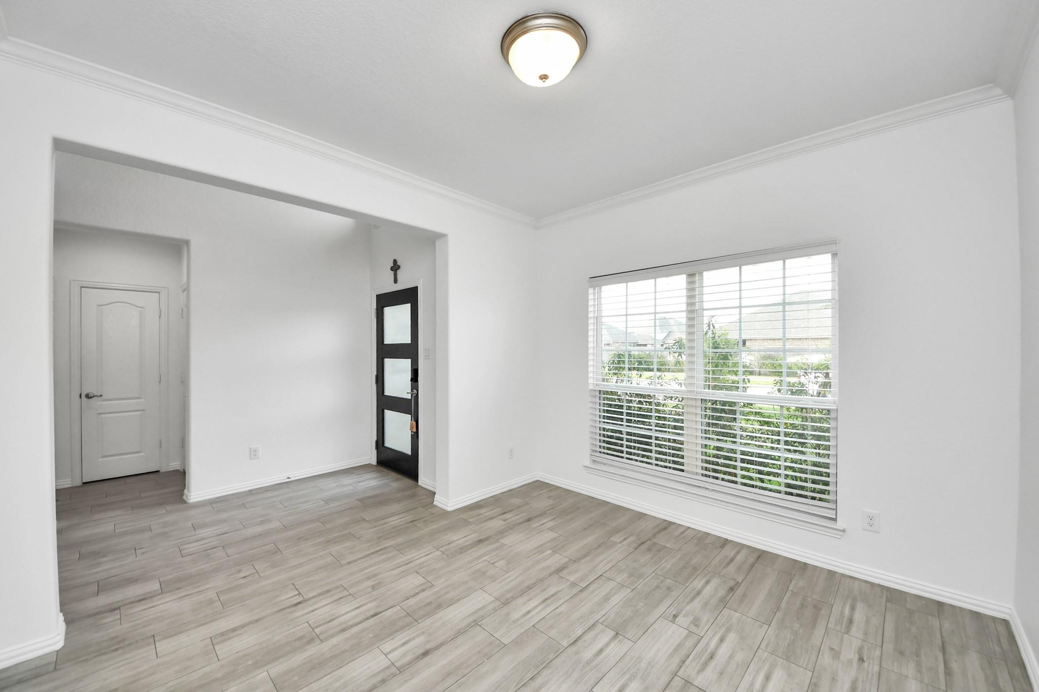 Empty living room with gray tile flooring, a large window, and a black front door.