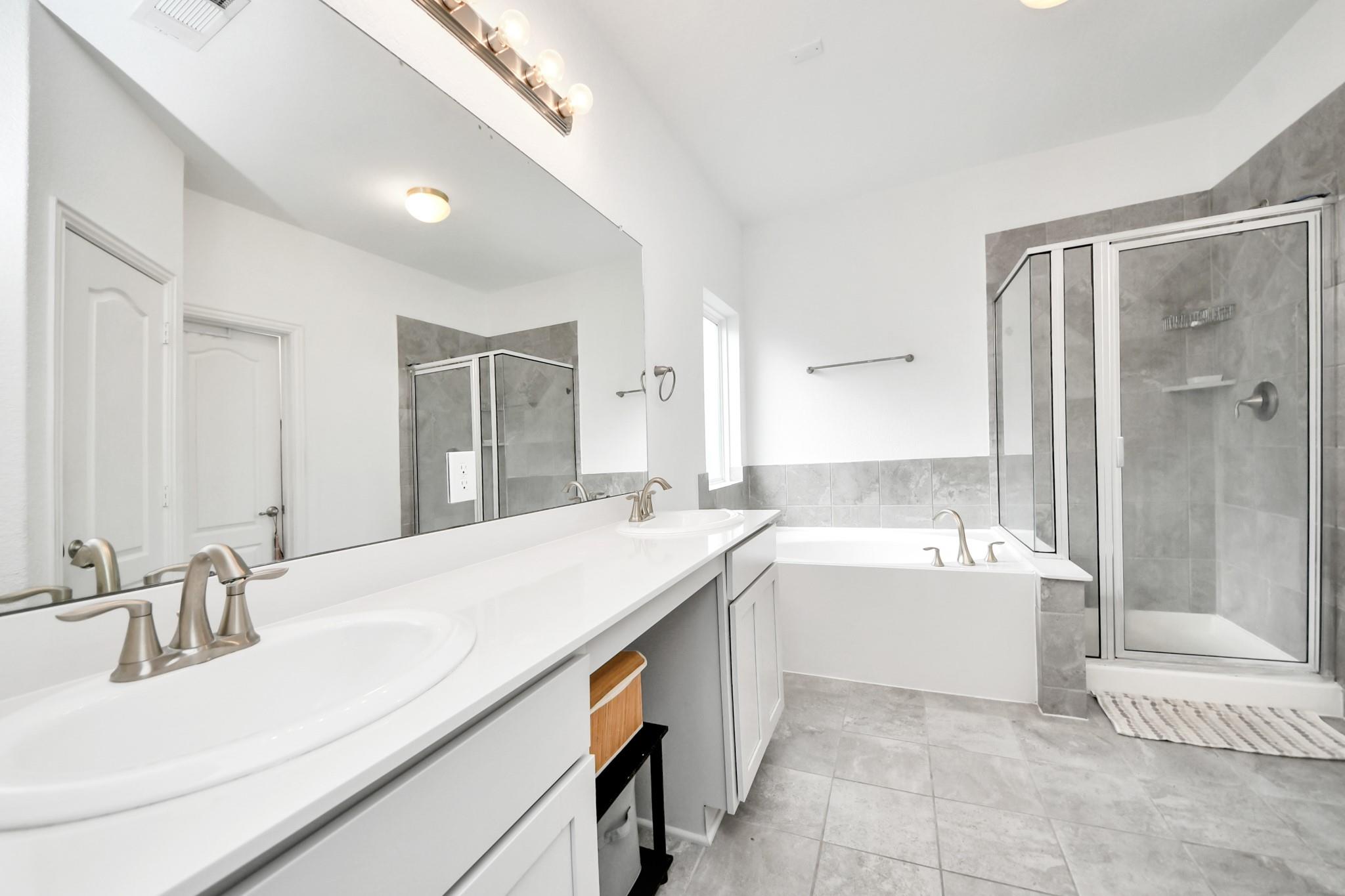 Bathroom with a long double-sink vanity, bathtub, and glass-enclosed shower.
