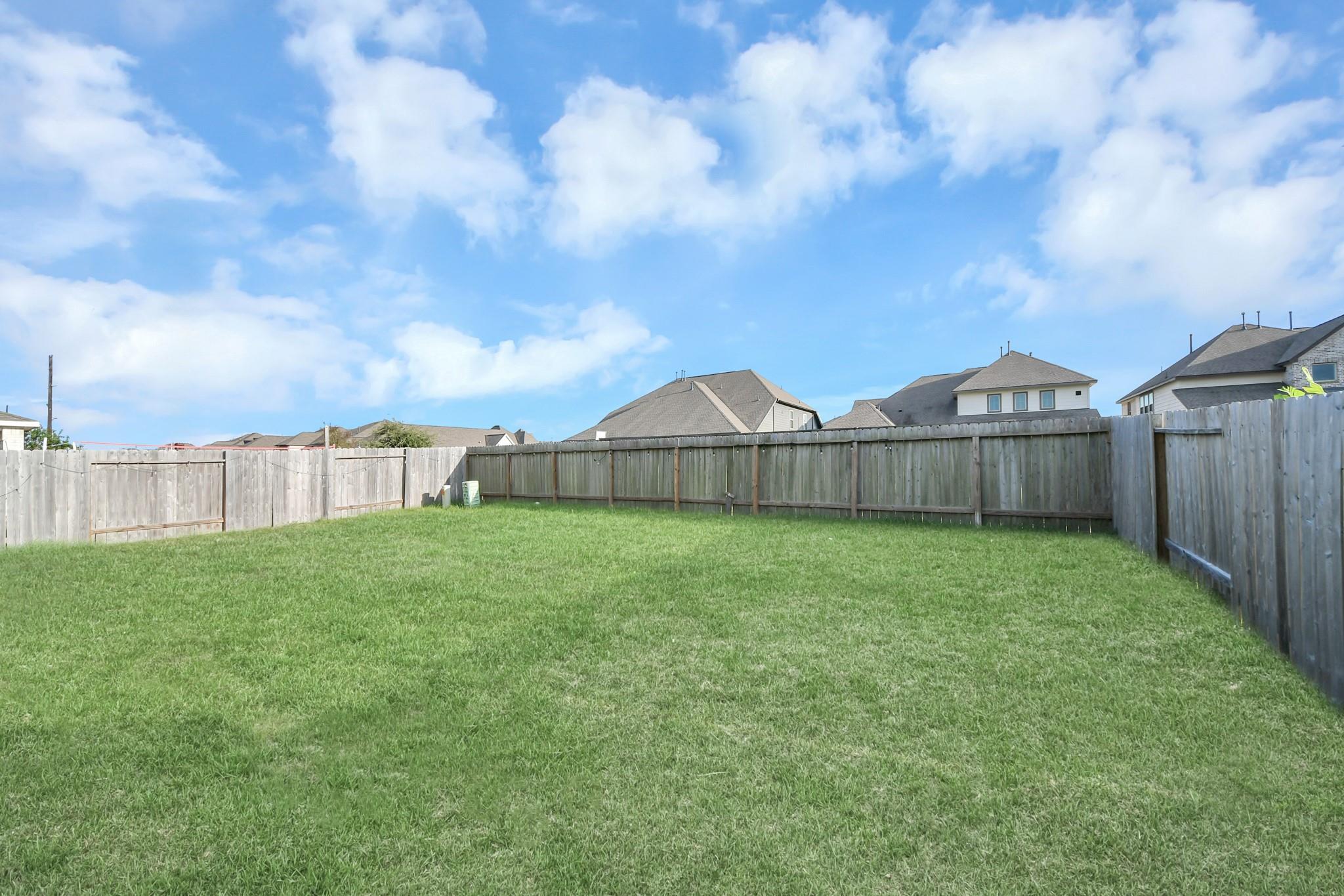 Fenced backyard with a broad grassy lawn and neighboring homes beyond the fence.
