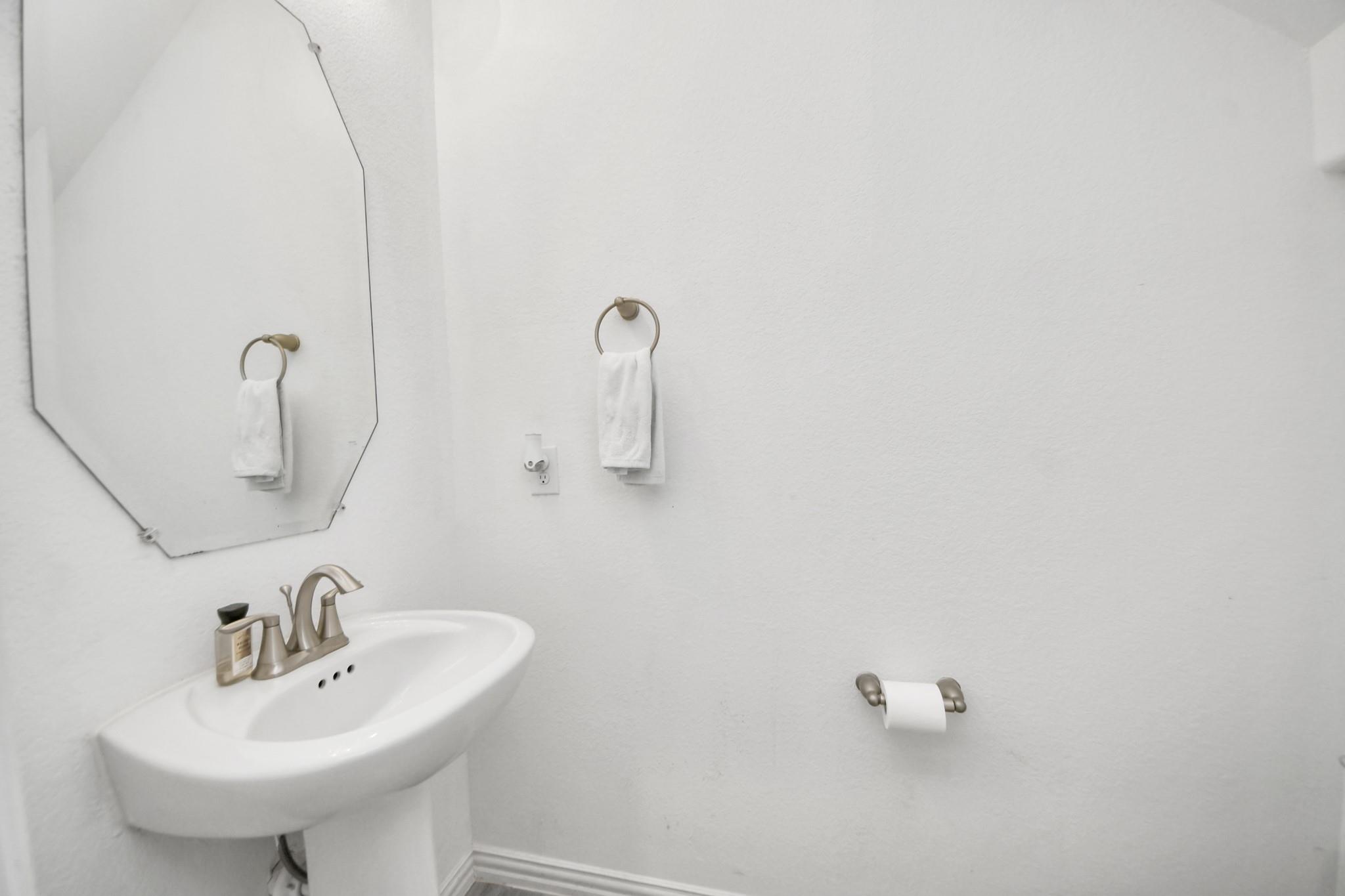 Bathroom with a white pedestal sink, large mirror, and hand towel on a wall ring.