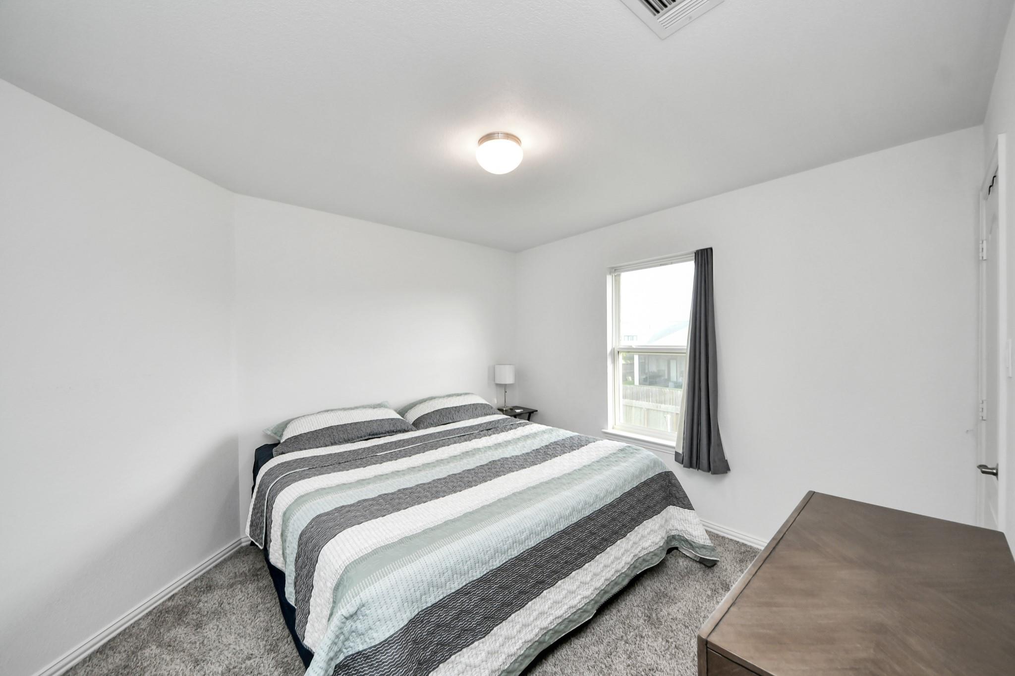Bedroom with striped bedding, gray carpet, and a window with a dark curtain.