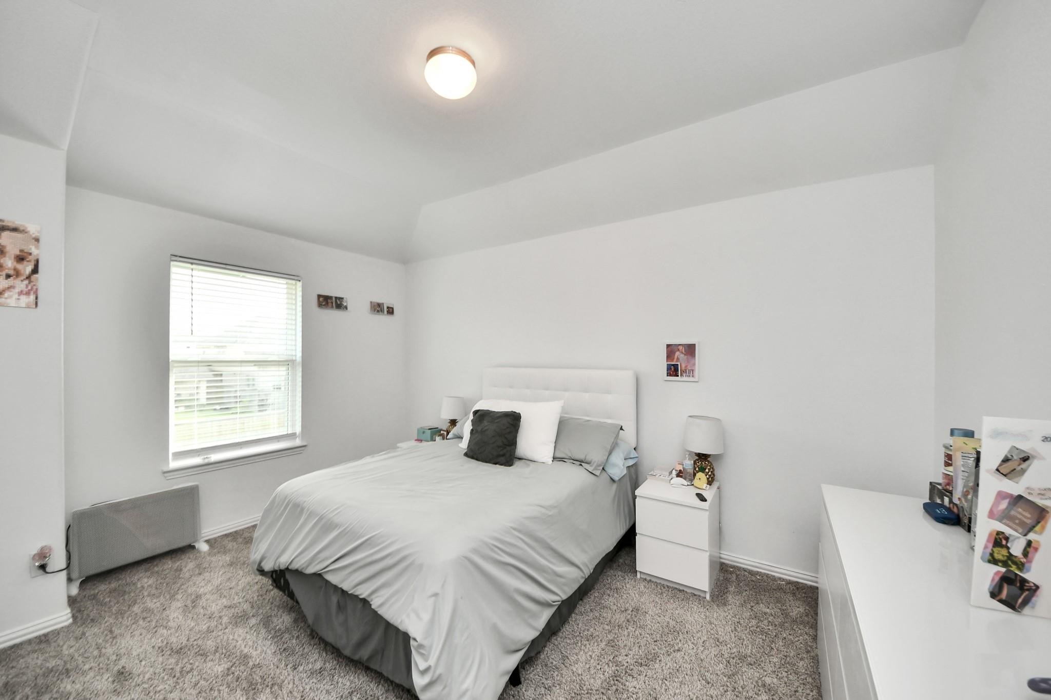Bedroom with a gray-and-white bed, white nightstands, and a window with blinds.