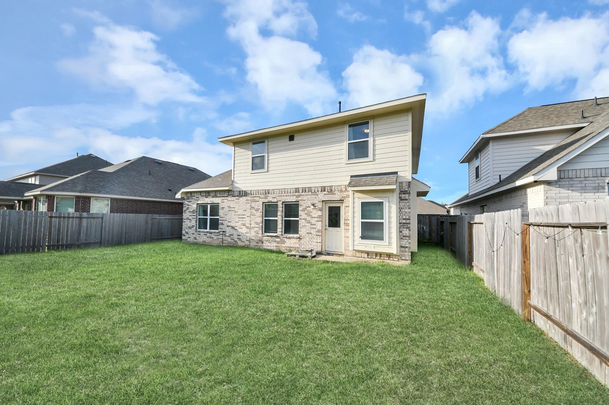 Two-story house with brick and light siding behind a broad fenced lawn.