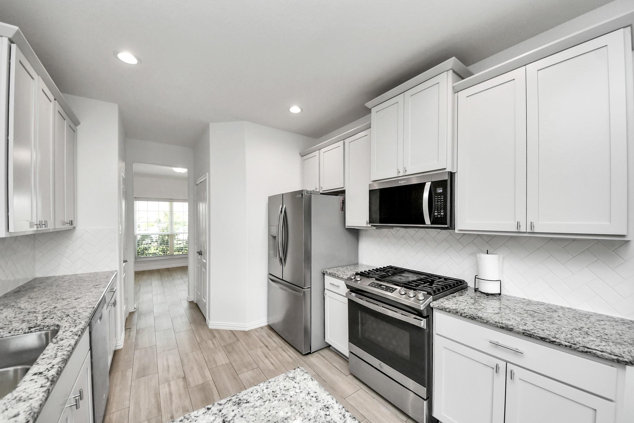 Modern kitchen with white cabinets, granite counters, stainless appliances, and a gas range.