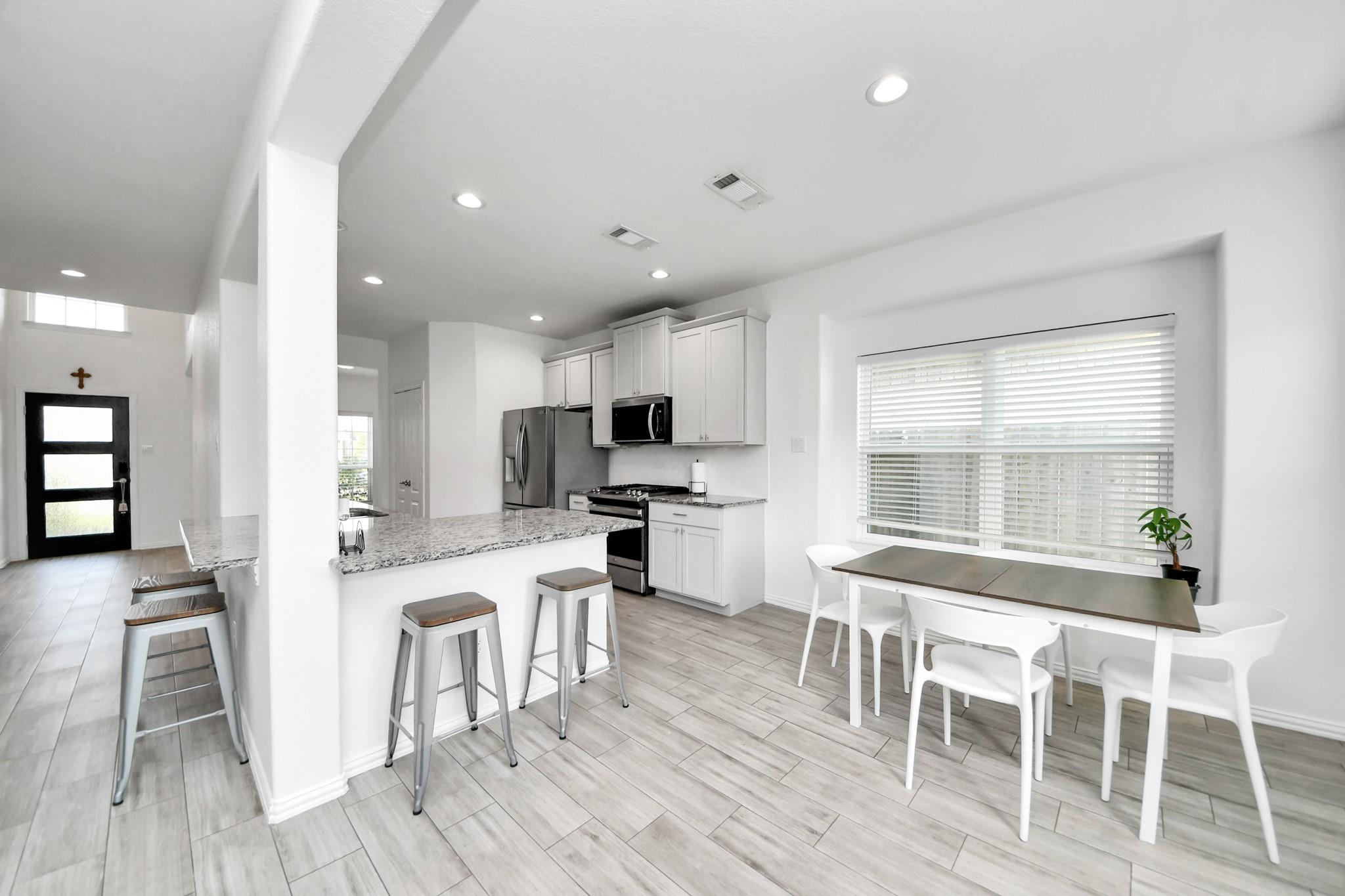 Open kitchen and dining area with a granite breakfast bar, stainless appliances, and gray tile floors.