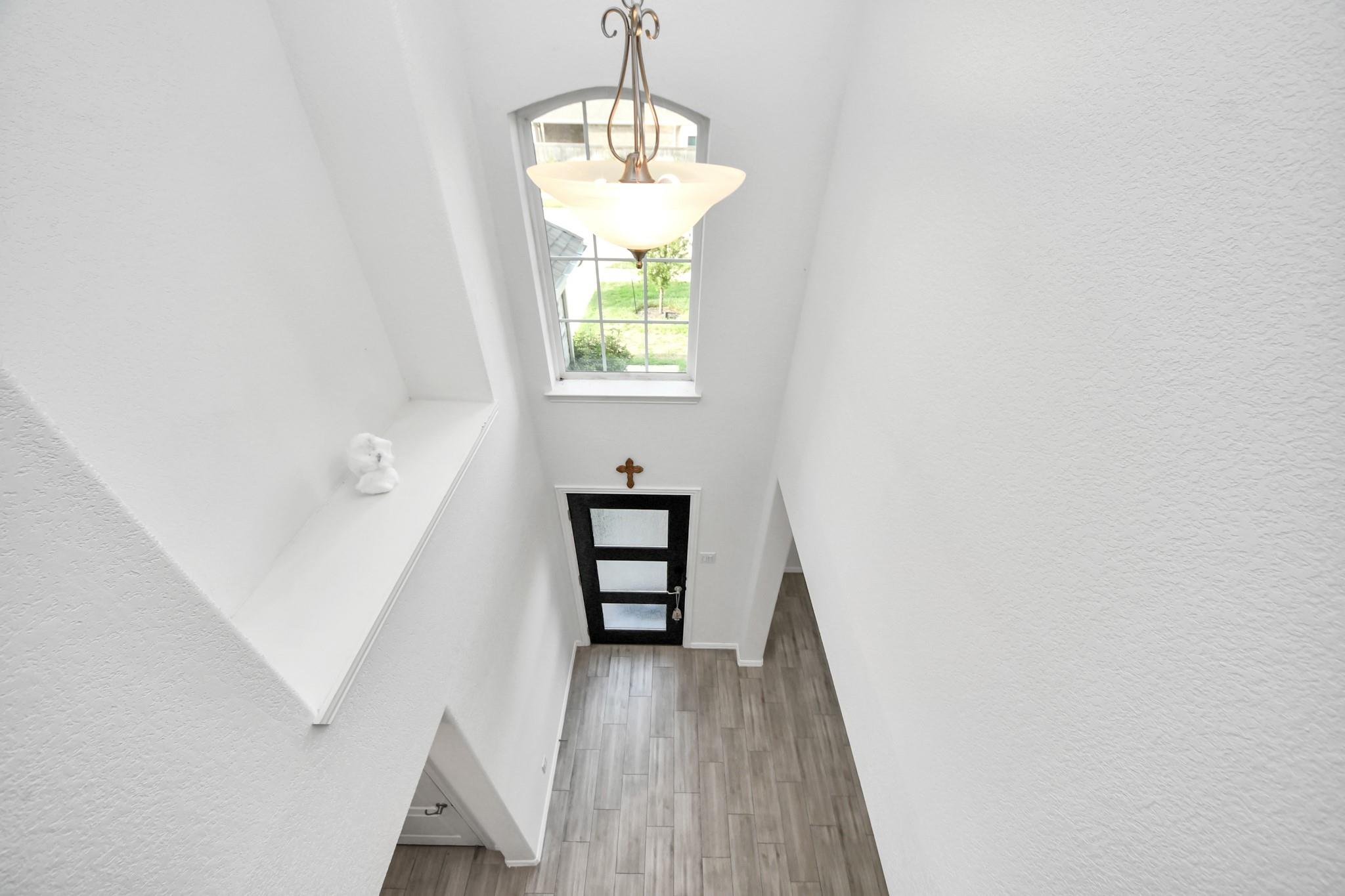 Two-story foyer with a tall window, hanging chandelier, black glass-panel front door, and gray tile flooring.