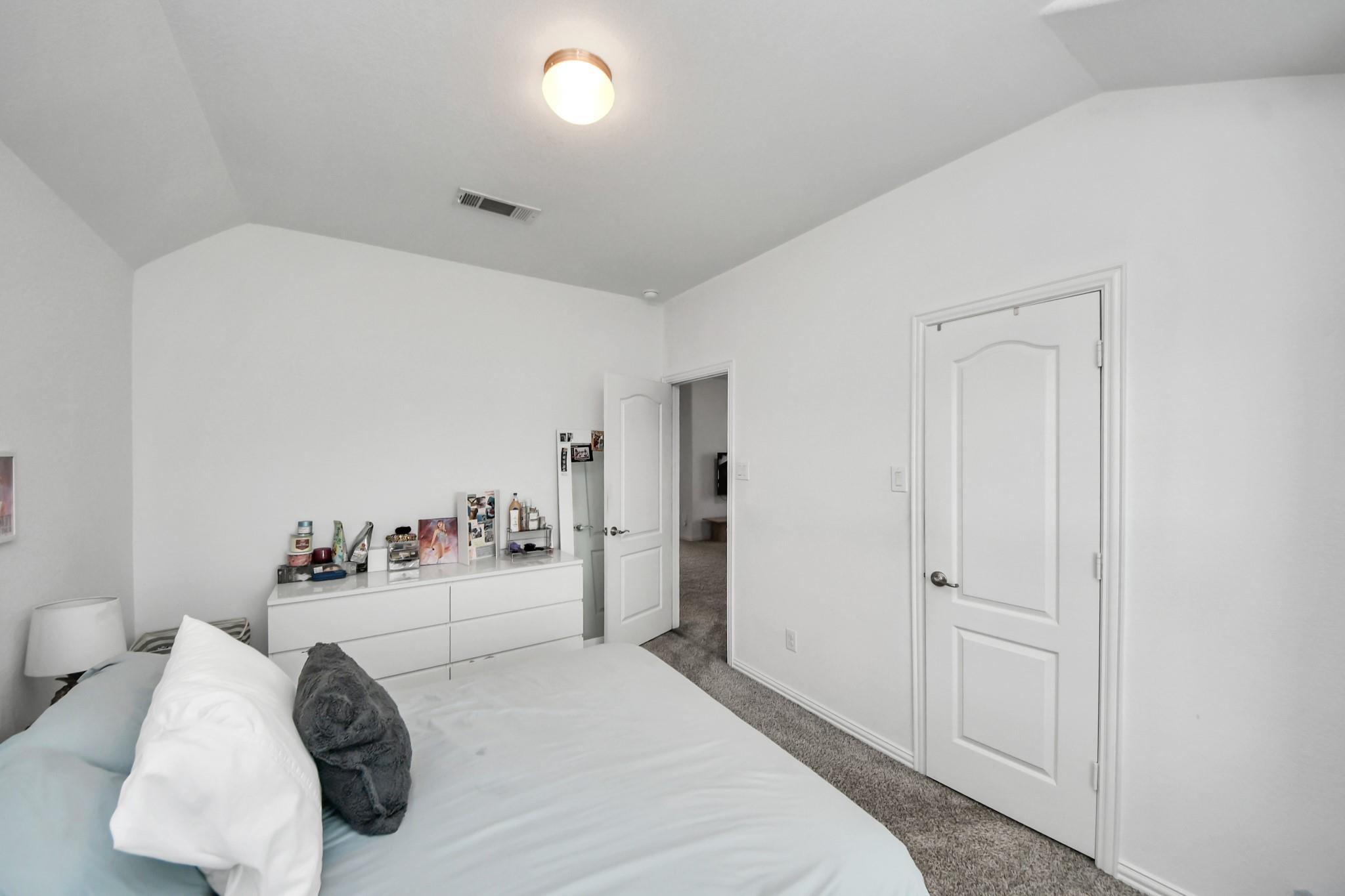 Furnished bedroom with a bed, white dresser, carpeted floor, and vaulted ceiling.