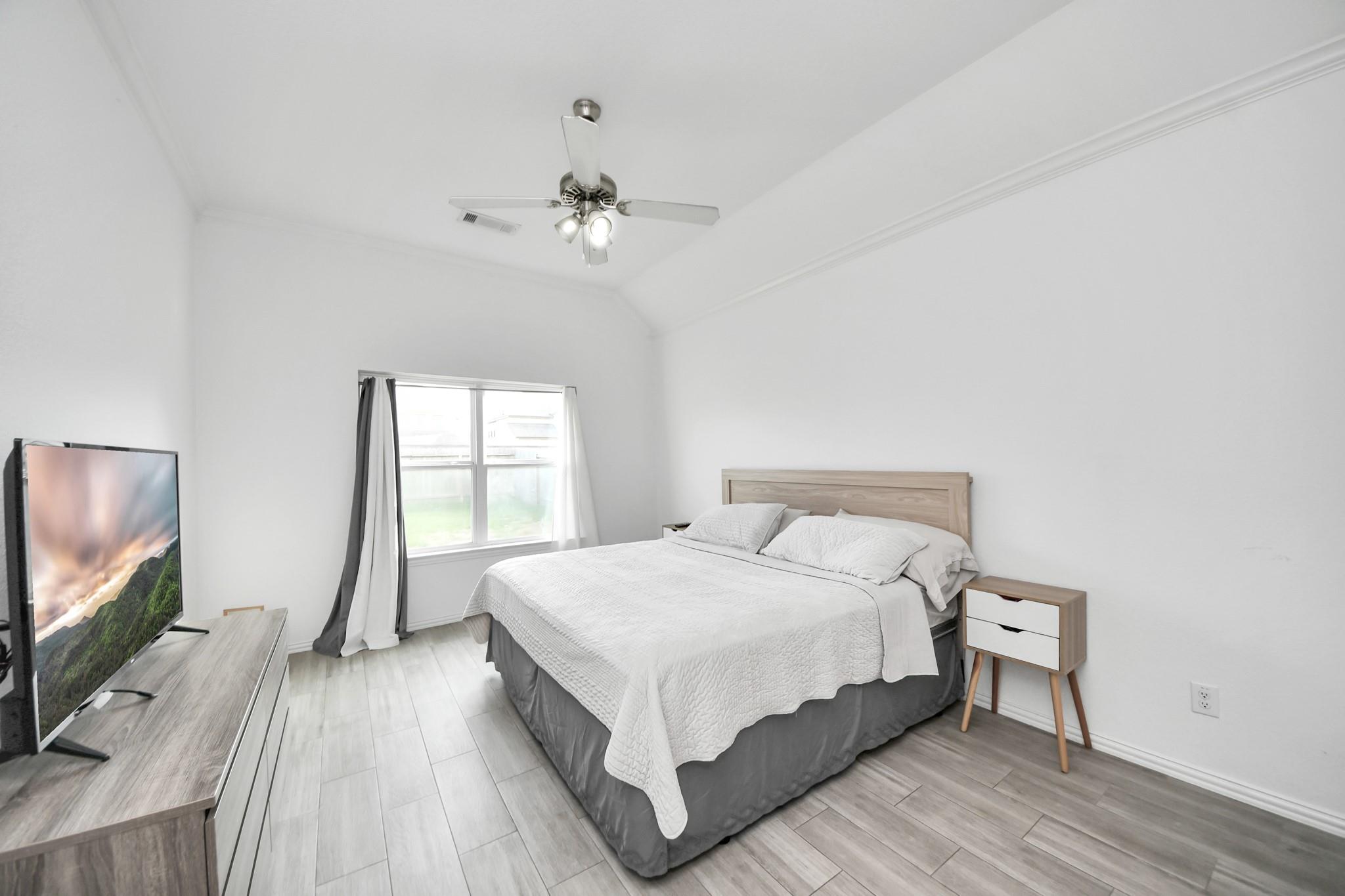 Furnished bedroom with a high ceiling, large curtained window, and neatly made bed.