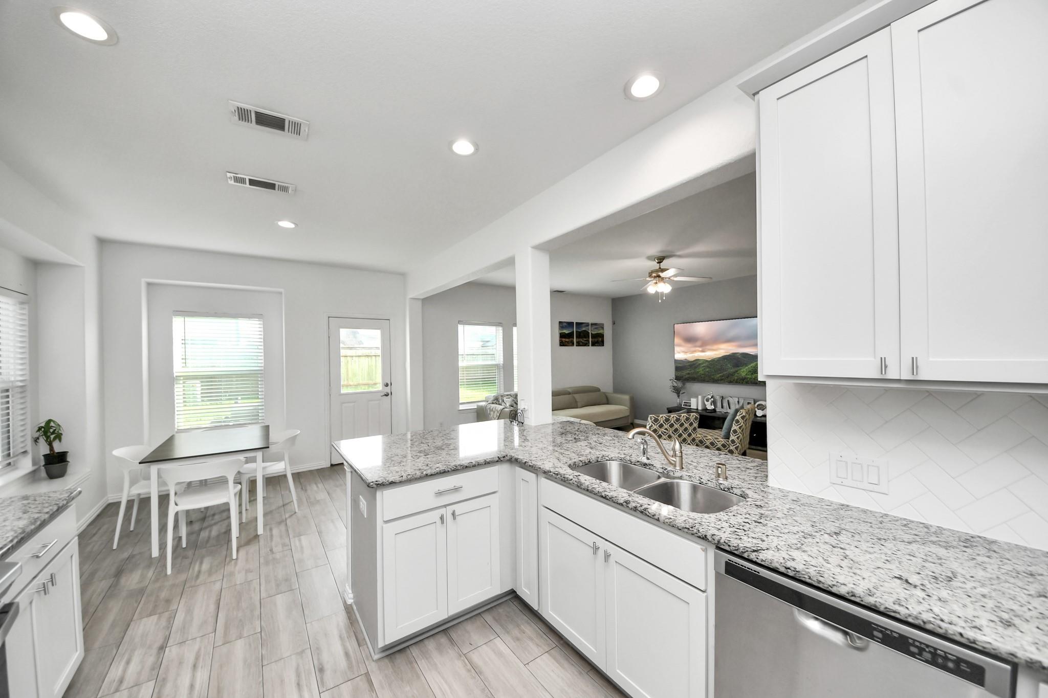 Open-plan kitchen with granite island and double sink overlooking a dining nook and furnished living area.