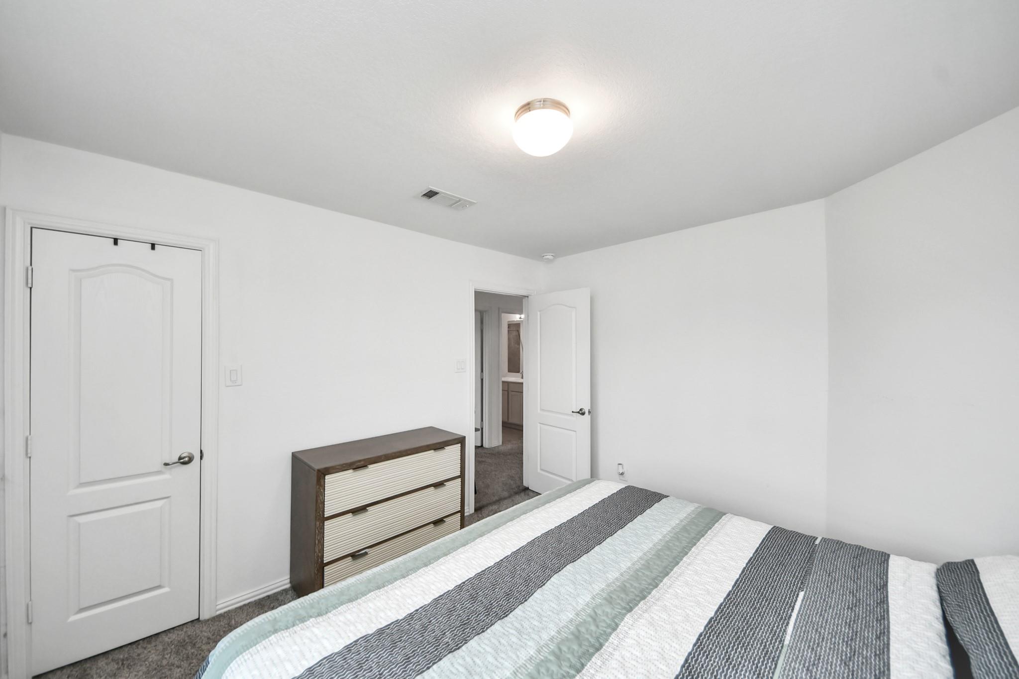 Bedroom with a striped bedspread, dark wood dresser, and white paneled doors.