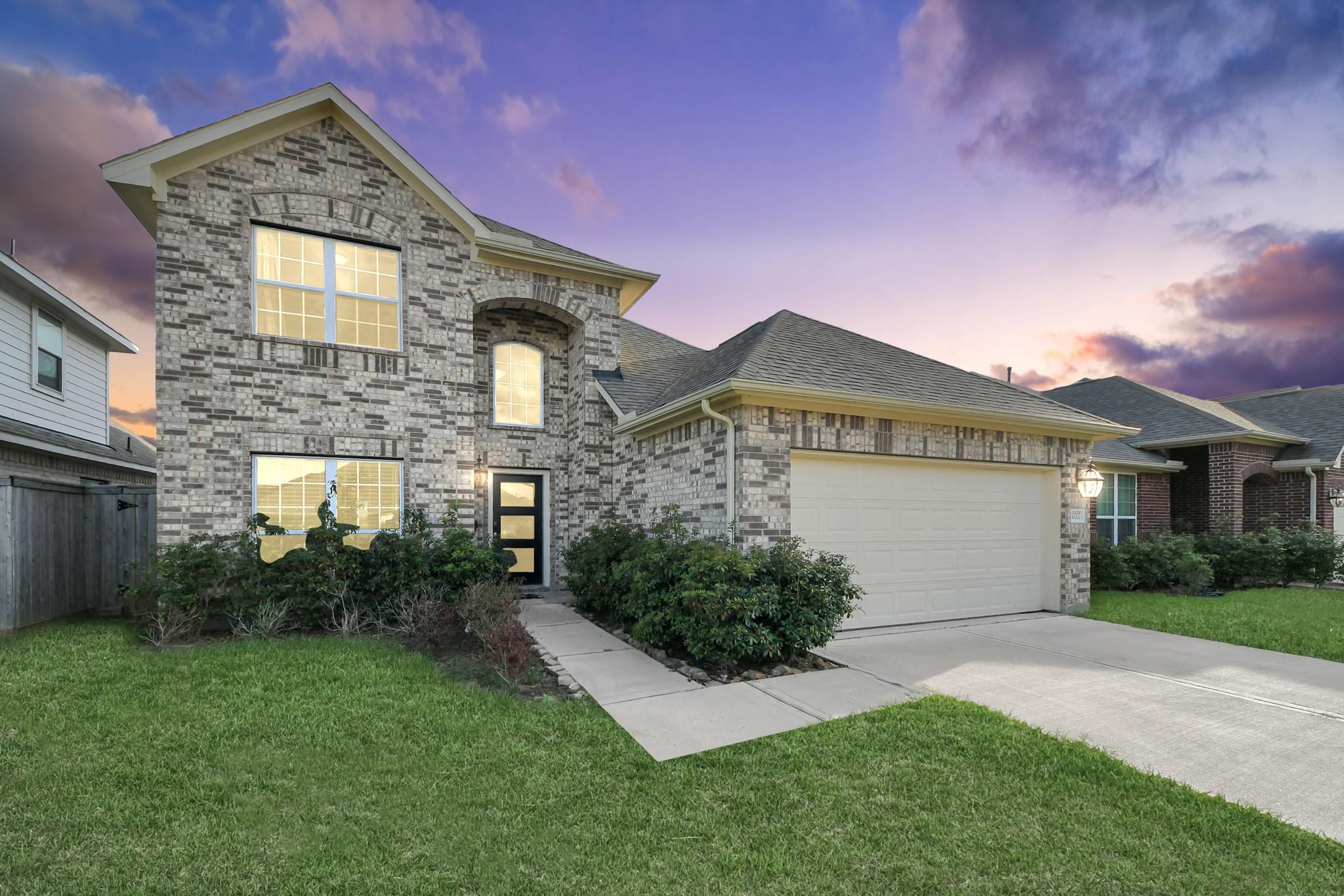 Two-story brick home with an attached garage, illuminated windows, and a front lawn at dusk.