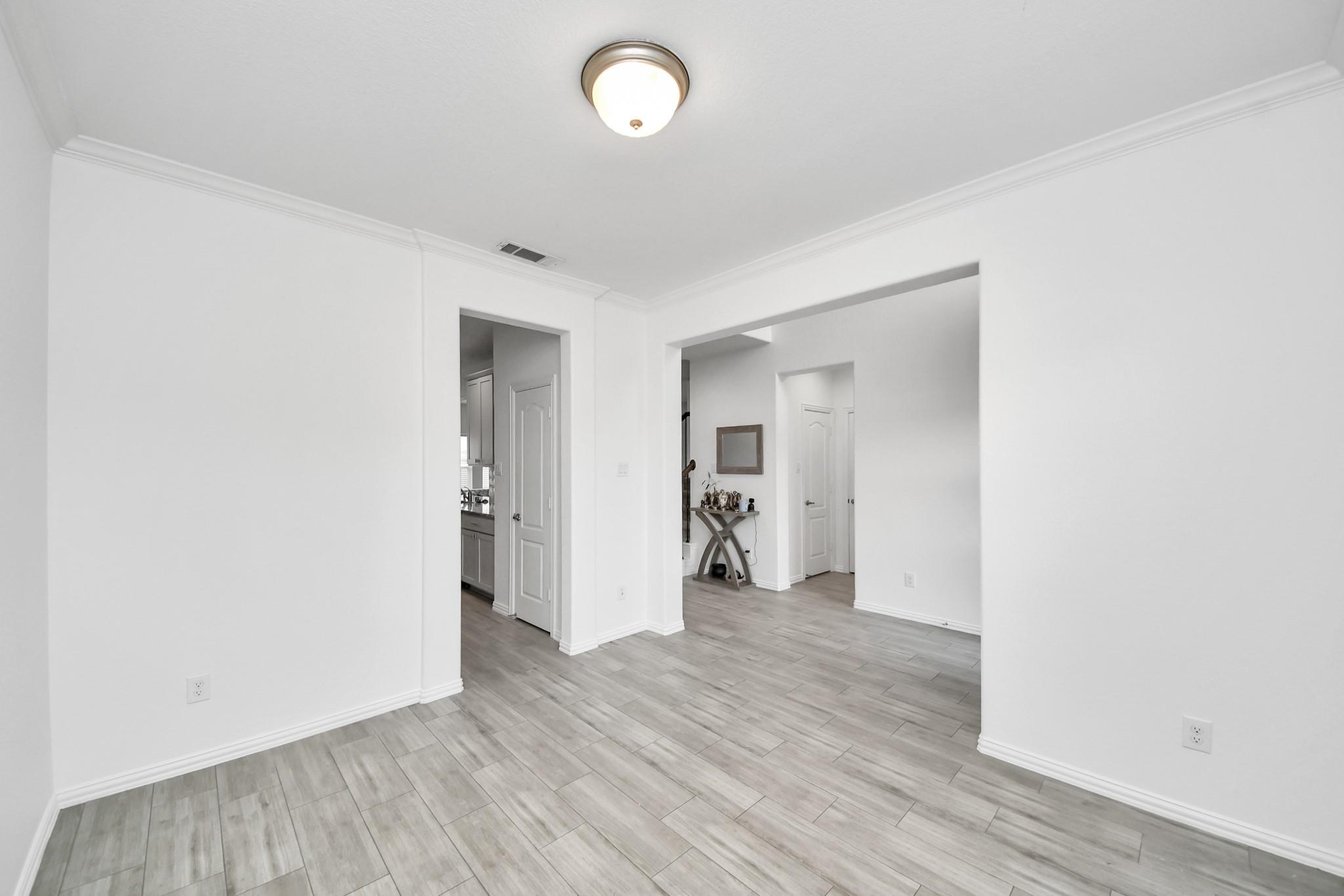 Empty interior room with gray tile flooring and open doorways to the kitchen and entry hall.