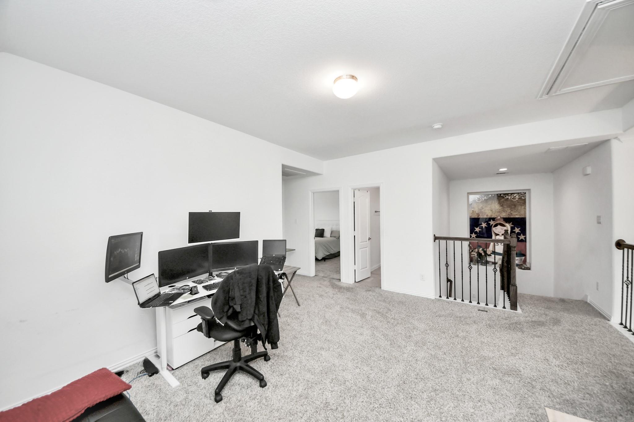 Upstairs loft office with a multi-monitor desk, carpeted floor, and stair railing.