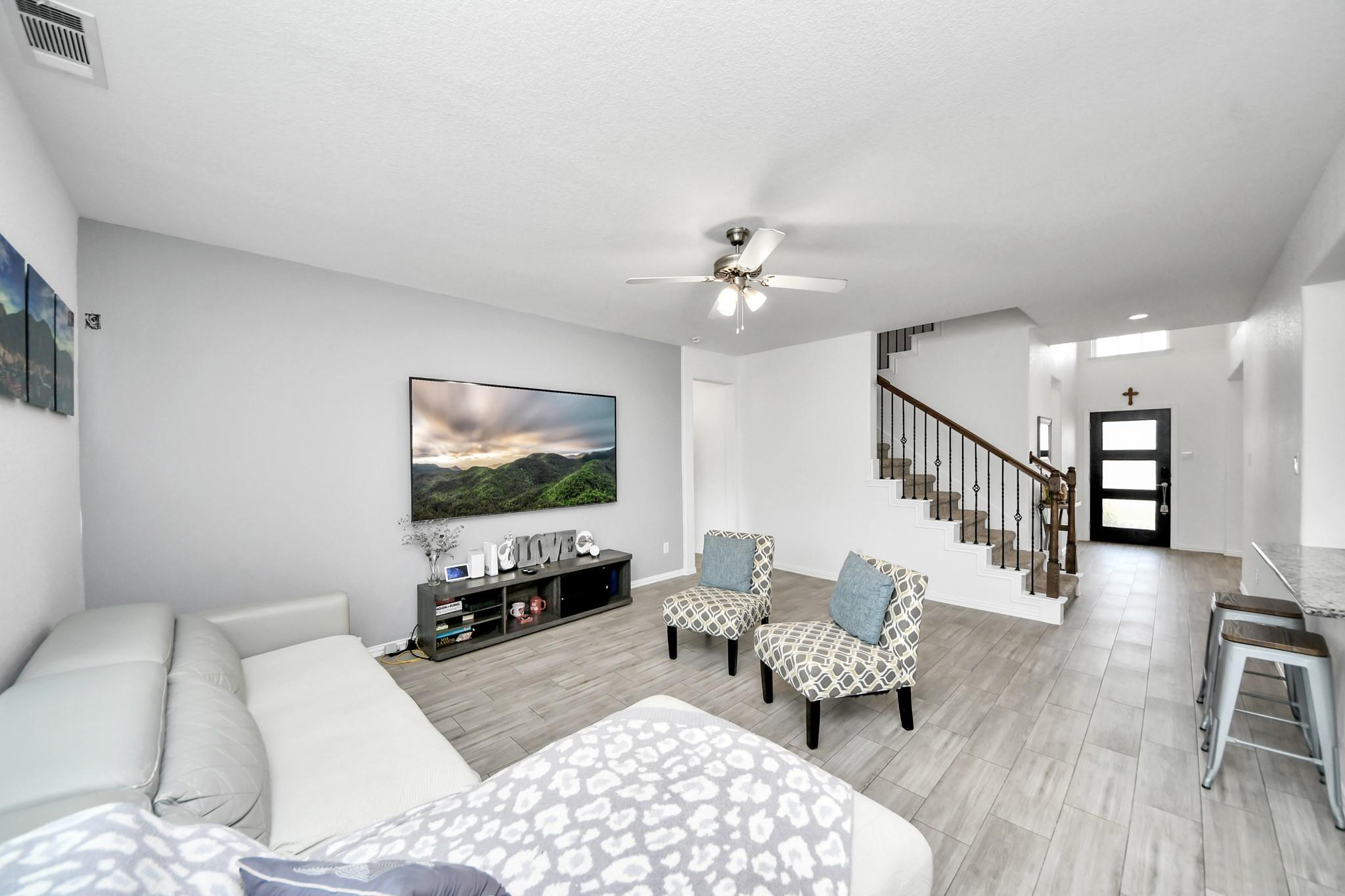 Furnished living room with a white sectional, patterned chairs, and an open staircase beside the entry.