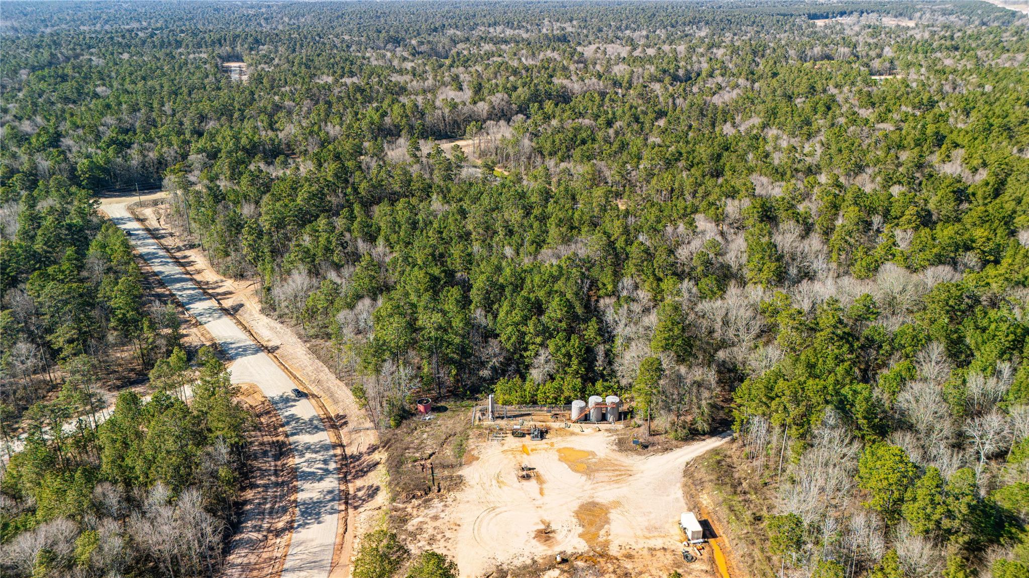 Aerial view of wooded land with a winding paved road and a cleared construction site.