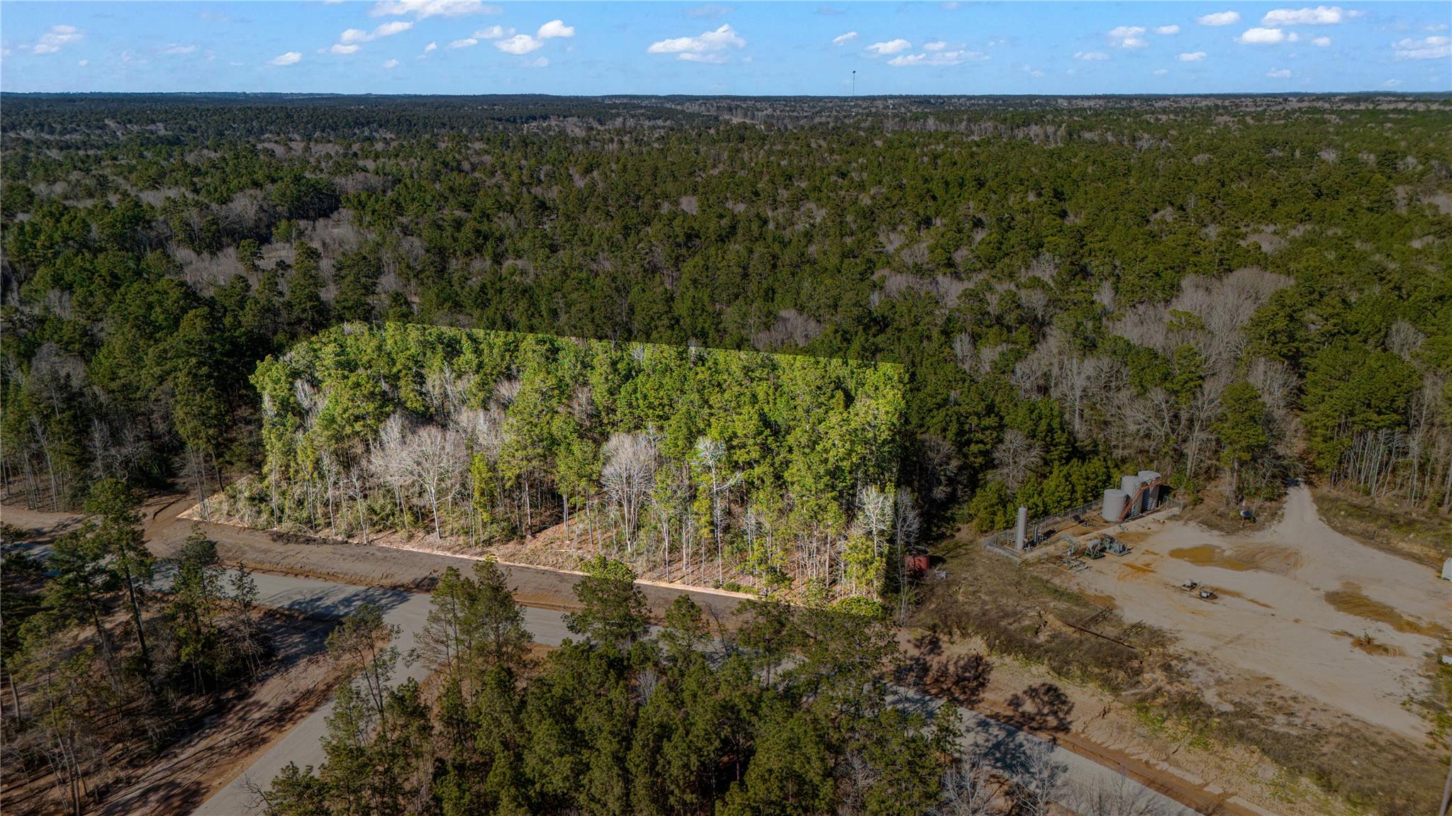 Aerial view of wooded land with winding access roads and a utility installation.