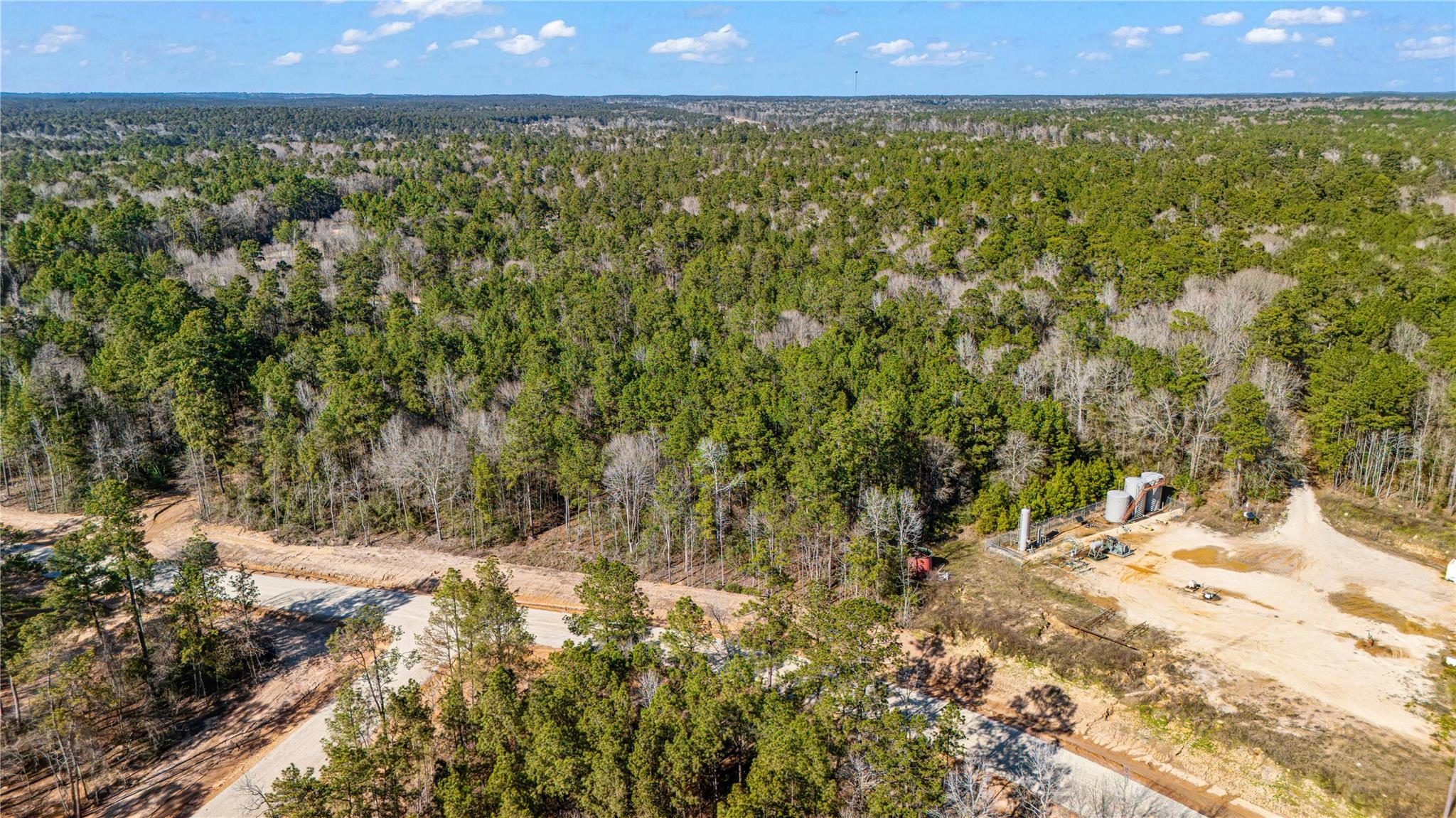 Aerial view of dense woodland with a dirt road and equipment in a cleared area.