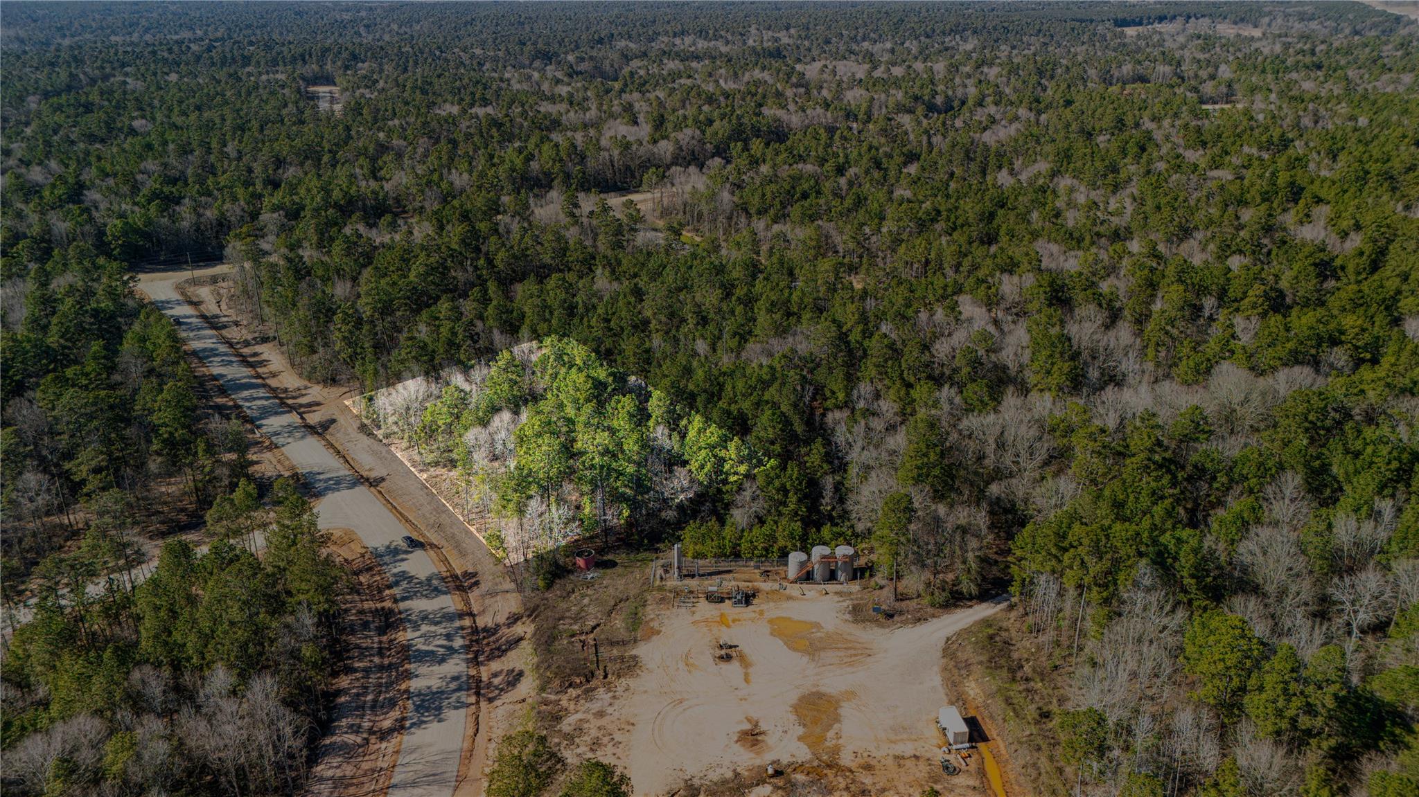Aerial view of wooded land beside a paved road, with a cleared construction area and equipment.