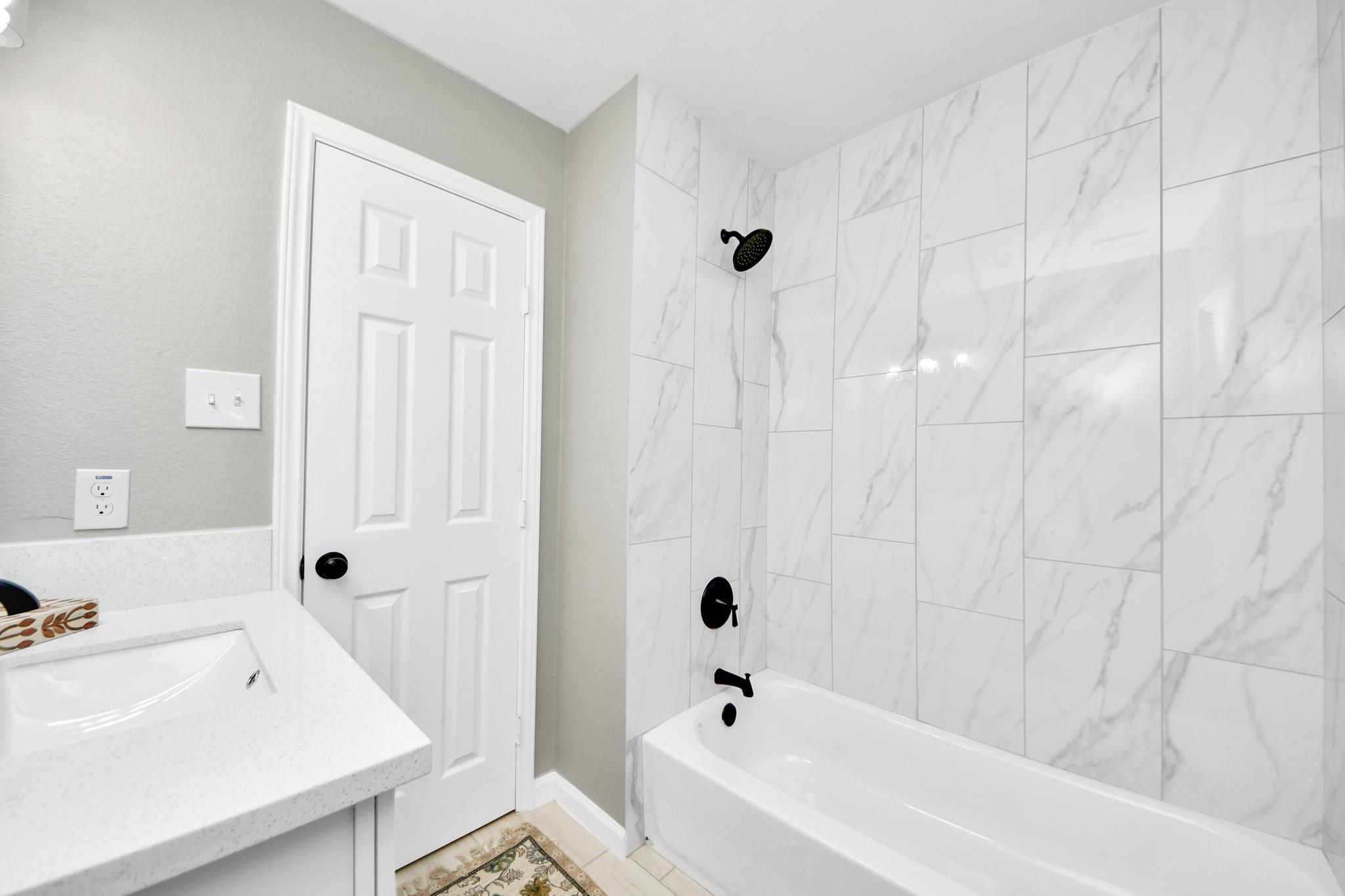 Bathroom with marble-look shower tile, matte black fixtures, and a white vanity and bathtub.