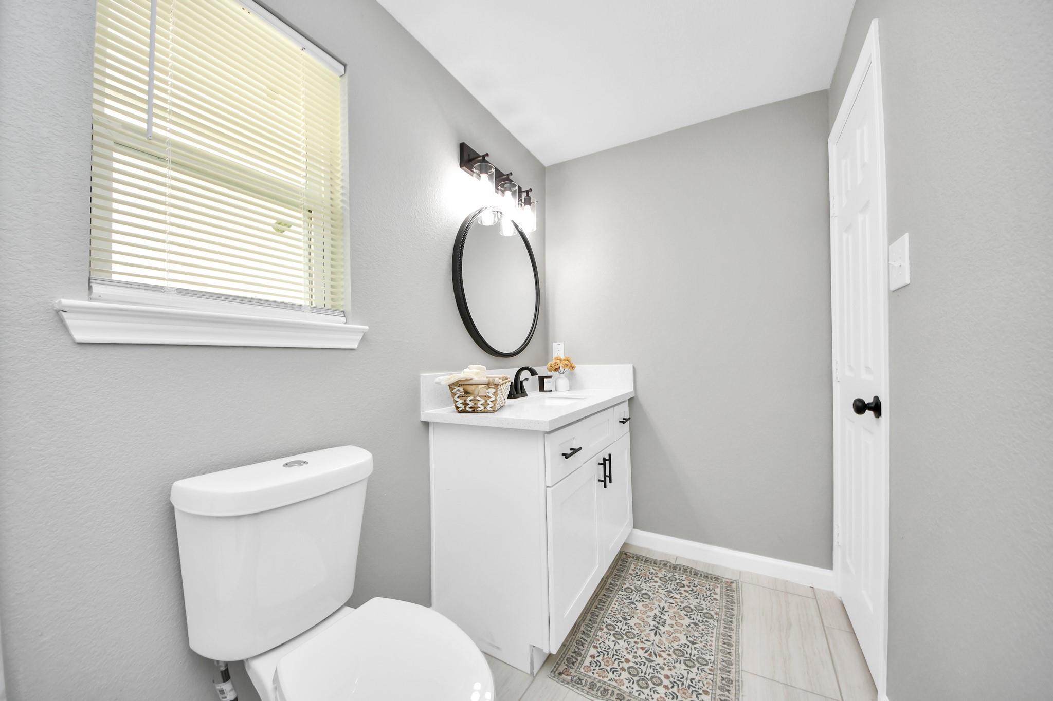Bathroom with a white vanity, black fixtures, oval mirror, and patterned floor runner.