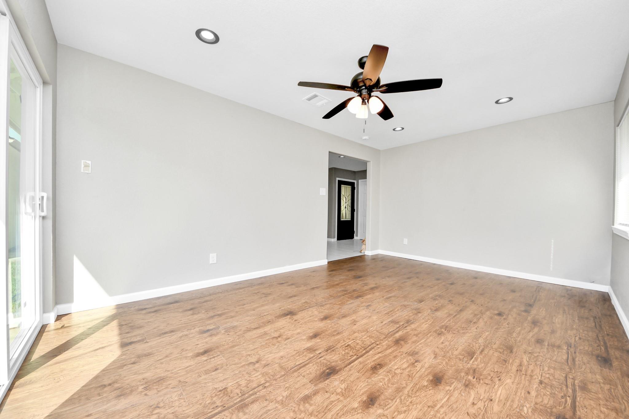Vacant living room with wood-look floors, ceiling fan, and sliding glass door.