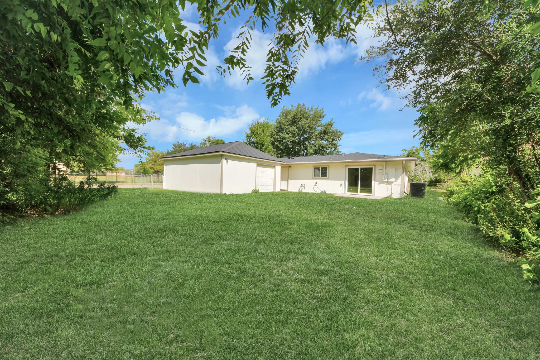 Rear of a single-story house with sliding glass doors, a broad lawn, and mature trees.