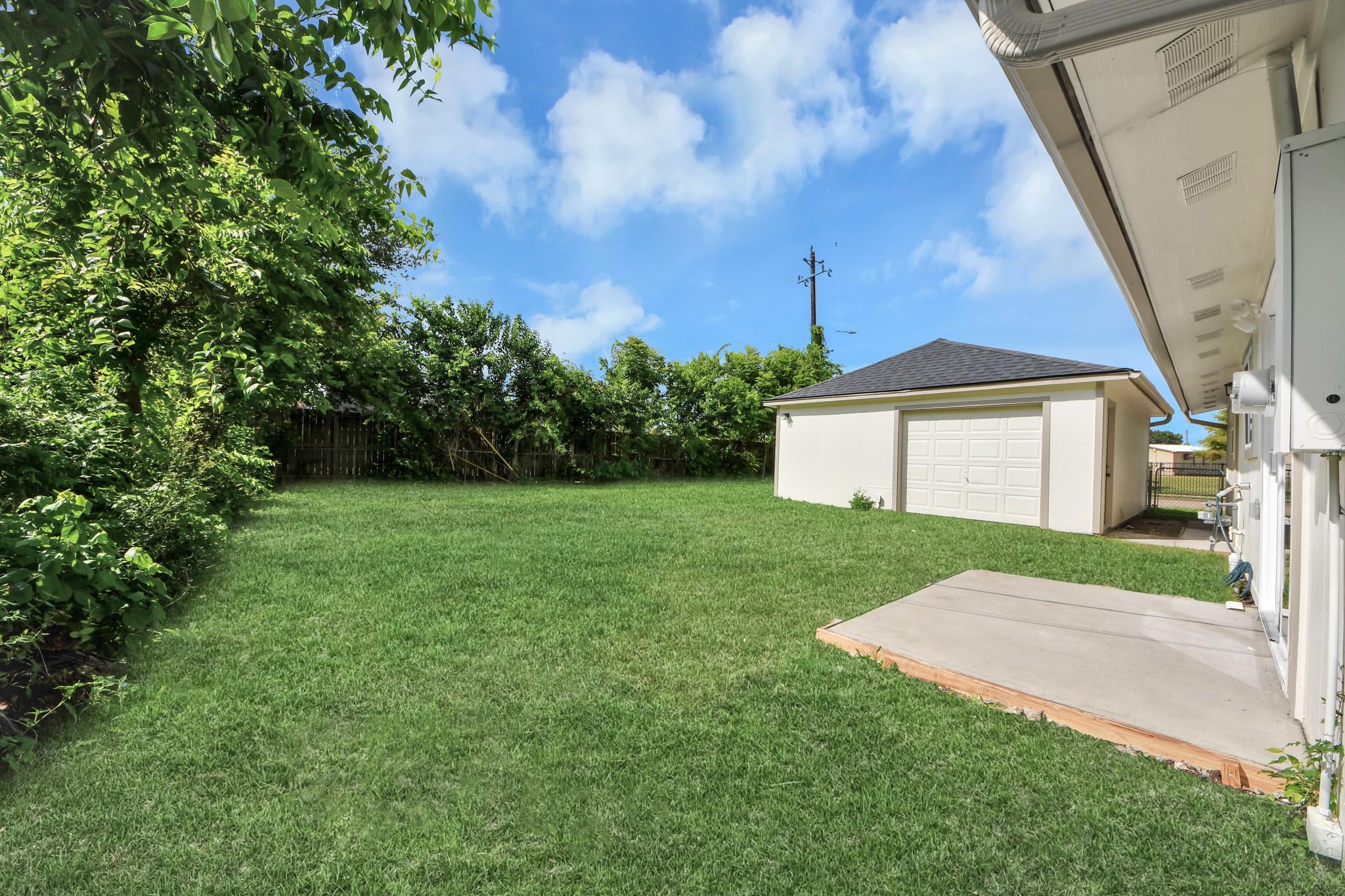 Grassy backyard with a concrete patio and detached garage beside the house.