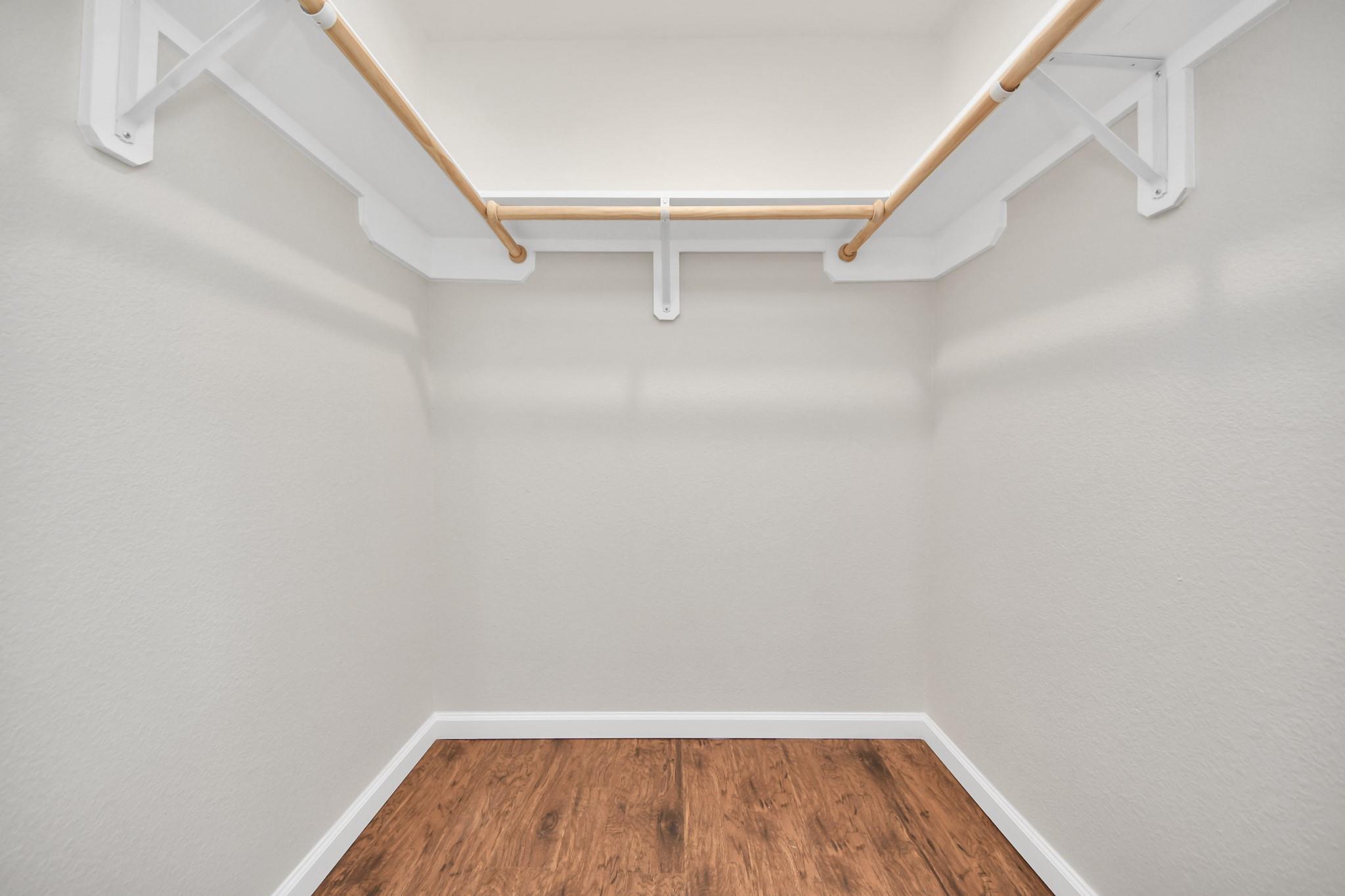 Empty walk-in closet with wooden hanging rods and wood-look flooring