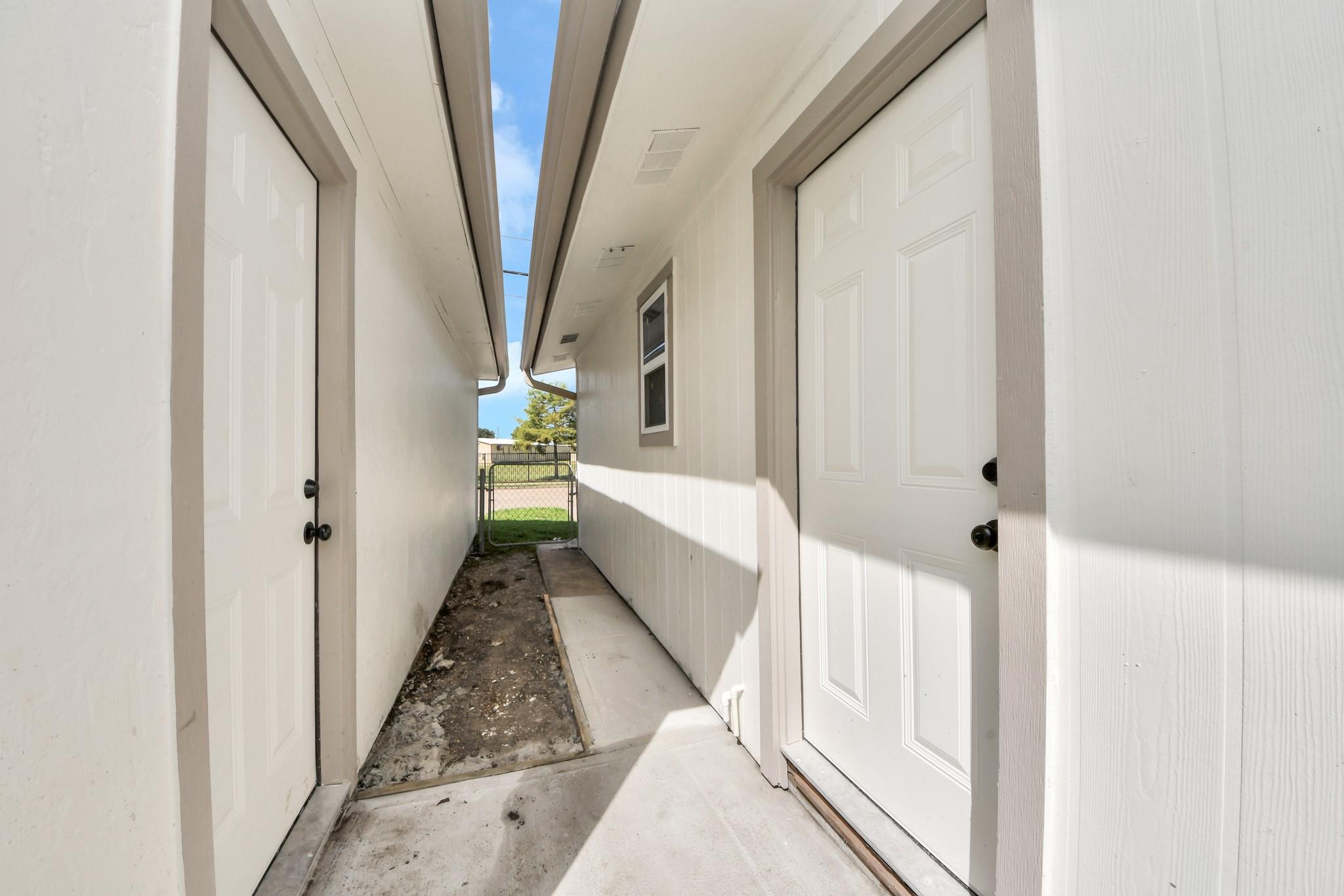 Narrow passage between white-sided house sections, ending at a metal gate to the yard.