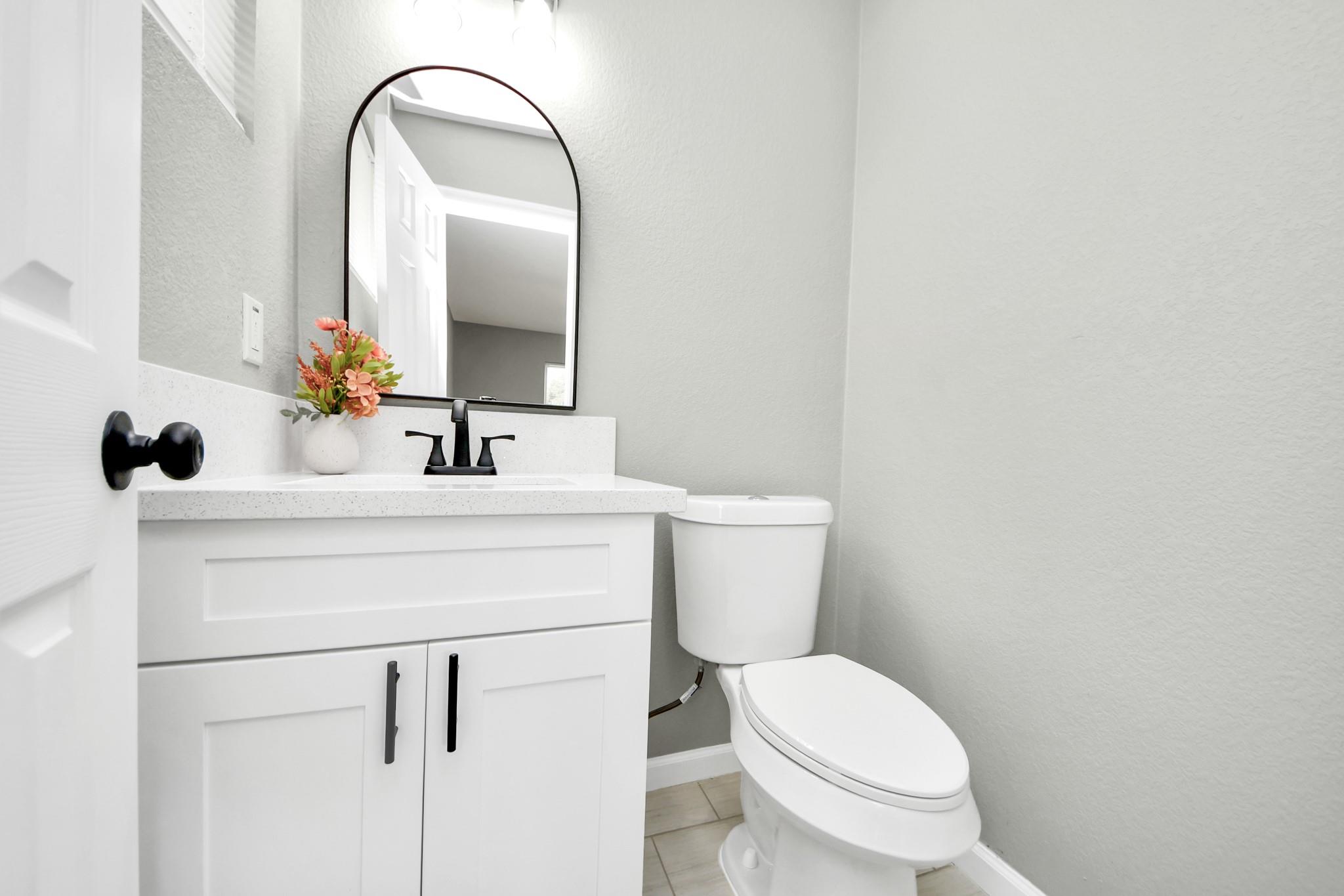 Bathroom with a white vanity, black fixtures, arched mirror, and toilet.
