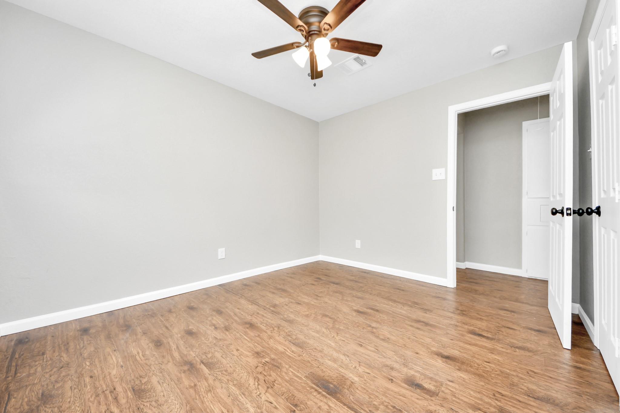 Empty bedroom with wood flooring, a ceiling fan, and an open closet doorway.