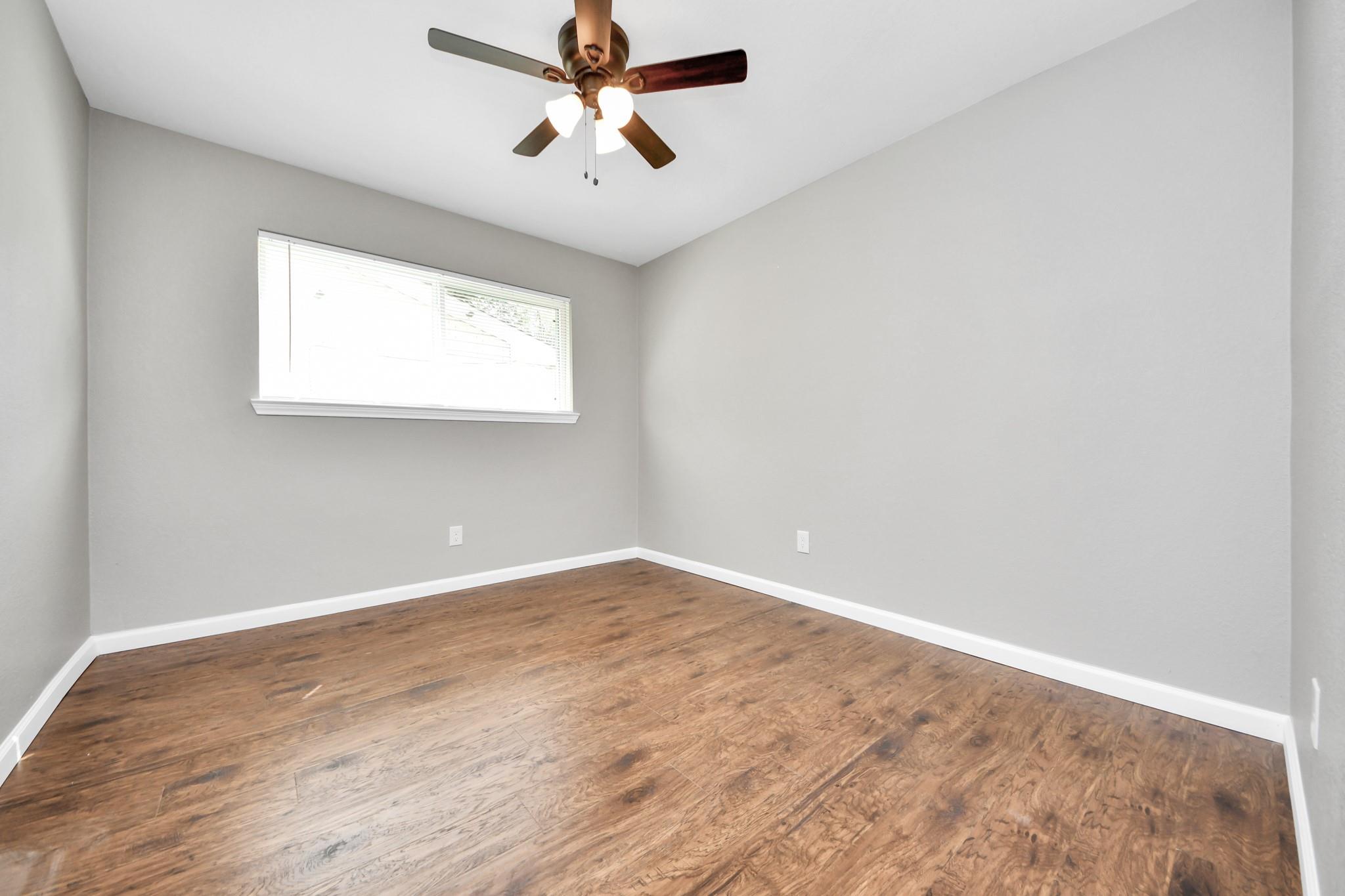 Empty bedroom with wood-look flooring, a window with blinds, and a ceiling fan.