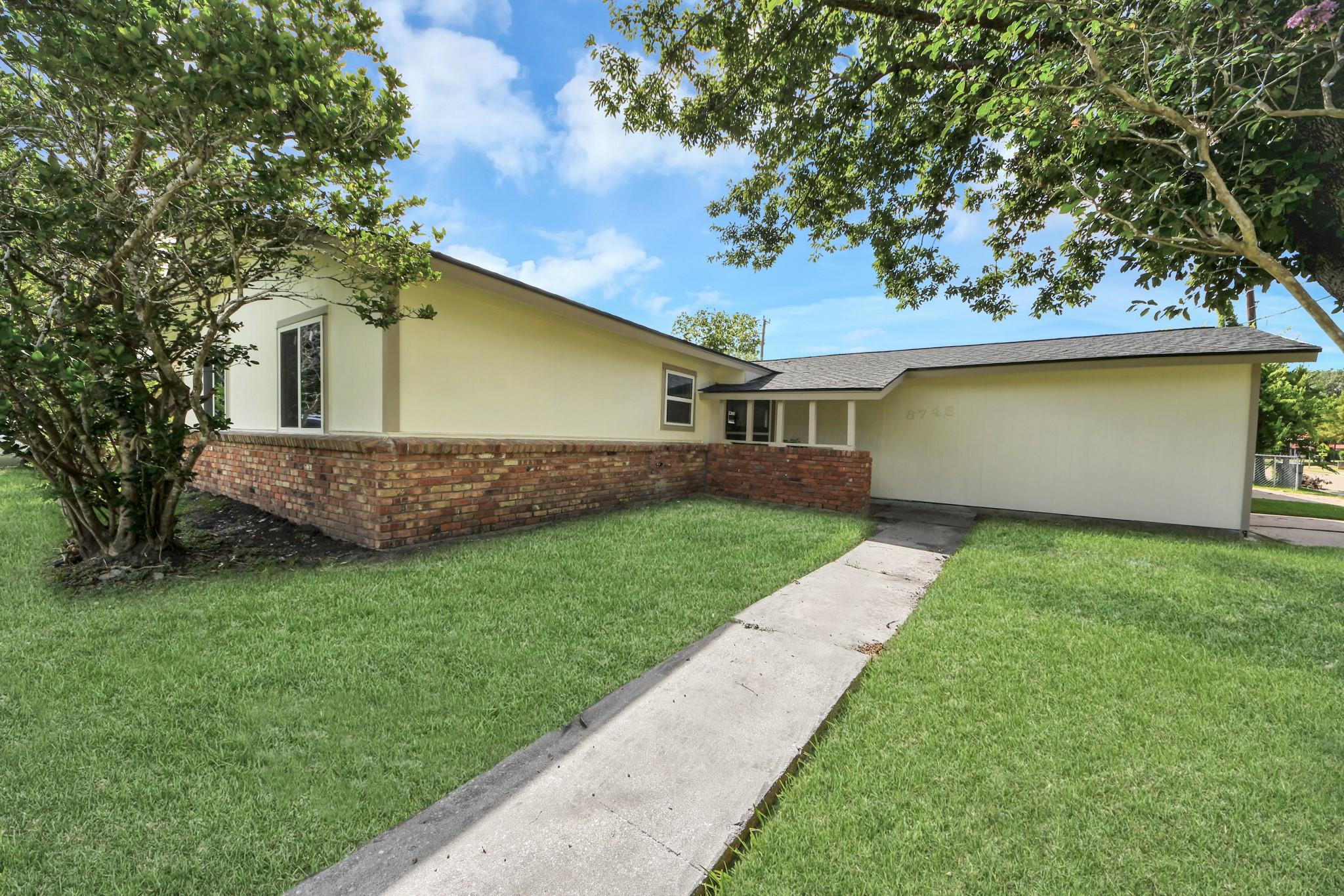 Single-story cream house with a brick front wall, broad lawn, and walkway to the entrance.