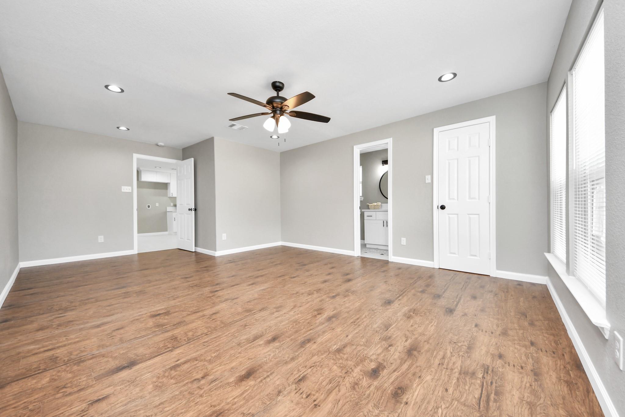 Empty bedroom with wood-look floors, a ceiling fan, and tall windows with blinds.