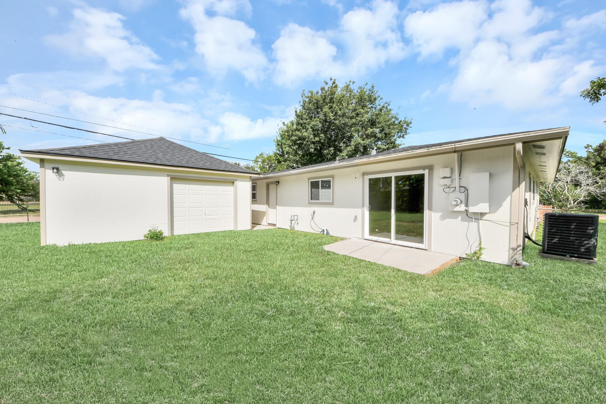Rear of a single-story house with an attached garage and sliding glass doors opening onto a broad lawn.