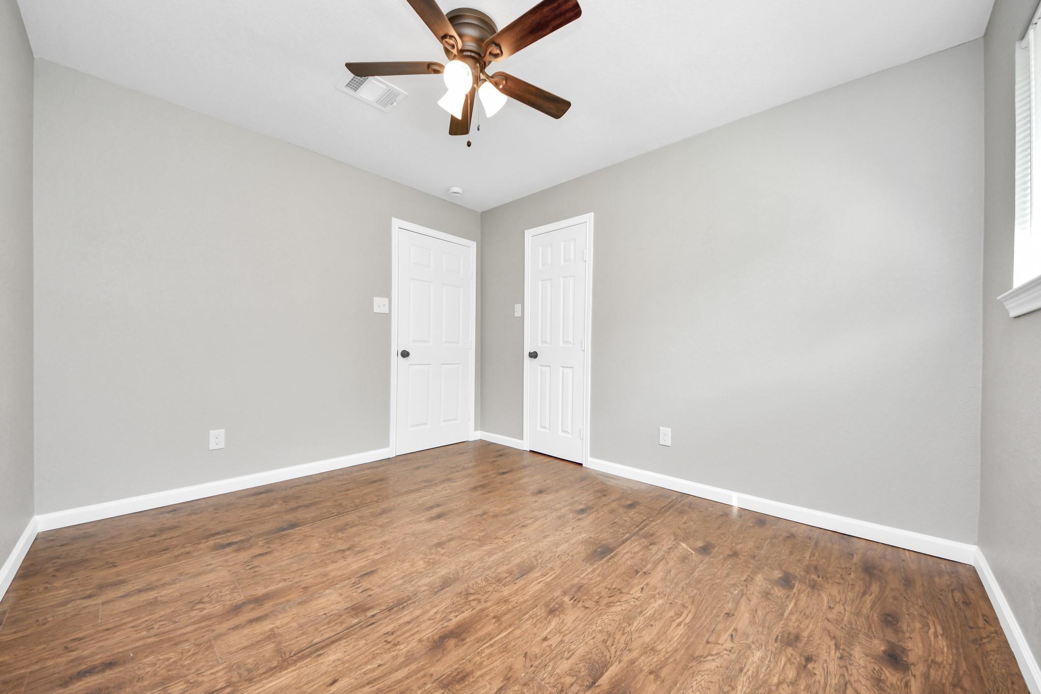 Empty bedroom with wood-look flooring, two white doors, and a ceiling fan.