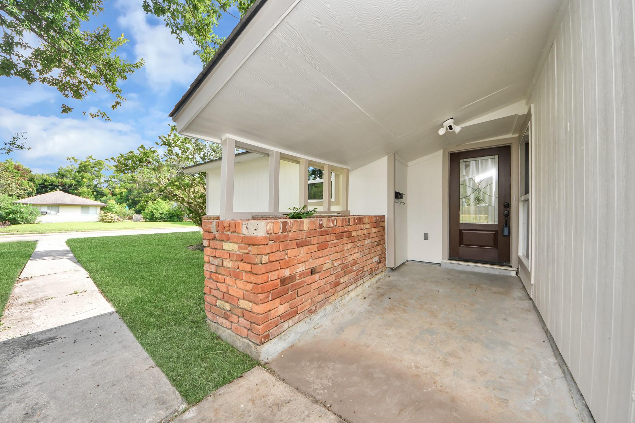 Covered front porch with a dark glass-panel door, low brick wall, and walkway.