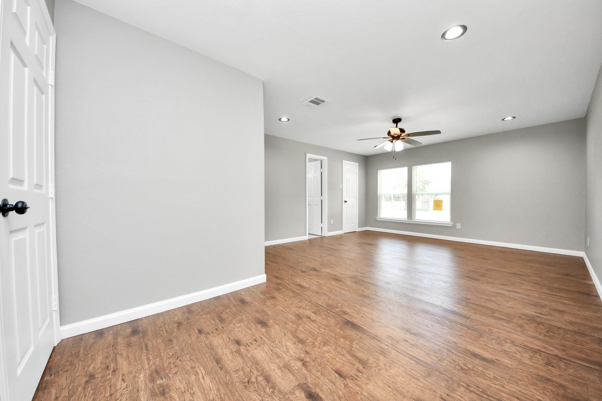 Empty living room with wood-look floors, two windows, and a ceiling fan with light.