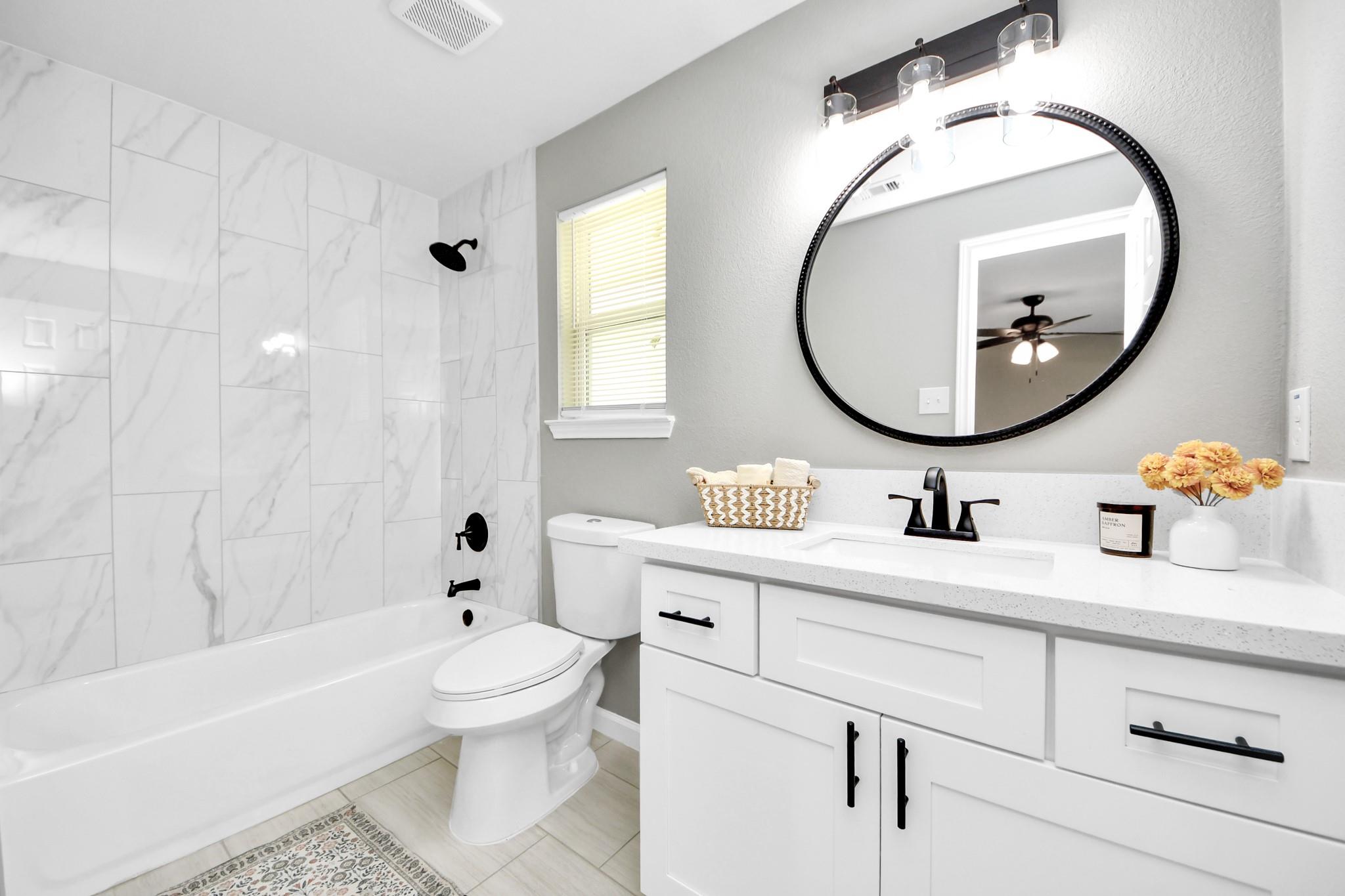 Bathroom with marble-look shower tile, black fixtures, and a white vanity beneath a round mirror.