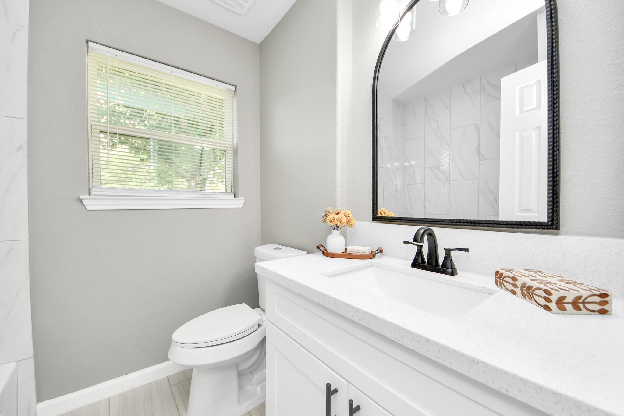 Bathroom vanity with a black faucet, large mirror, and window with blinds.