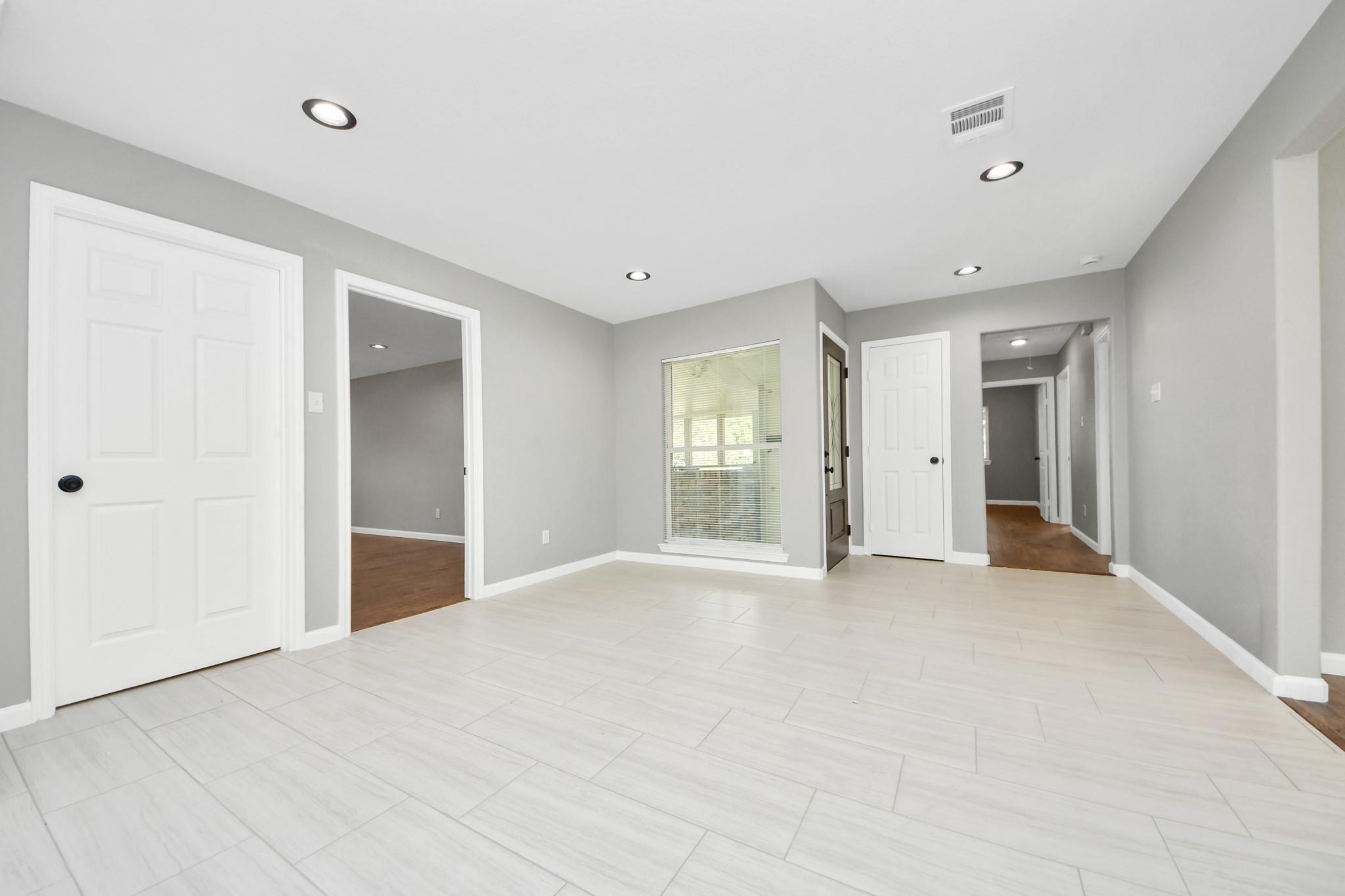 Vacant room with pale tile floors, gray walls, recessed lights, and a window with blinds.