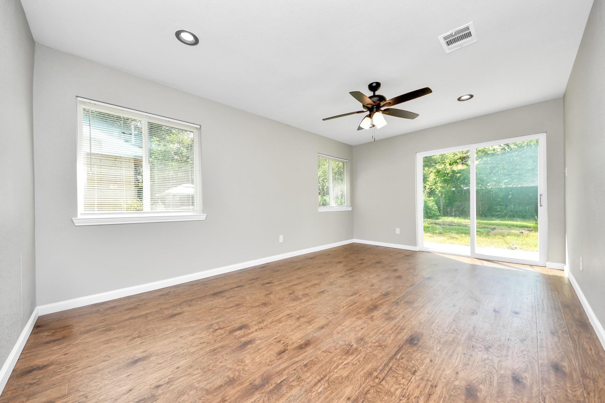 Empty living room with wood-look floors, a ceiling fan, and a sliding glass door to the yard.