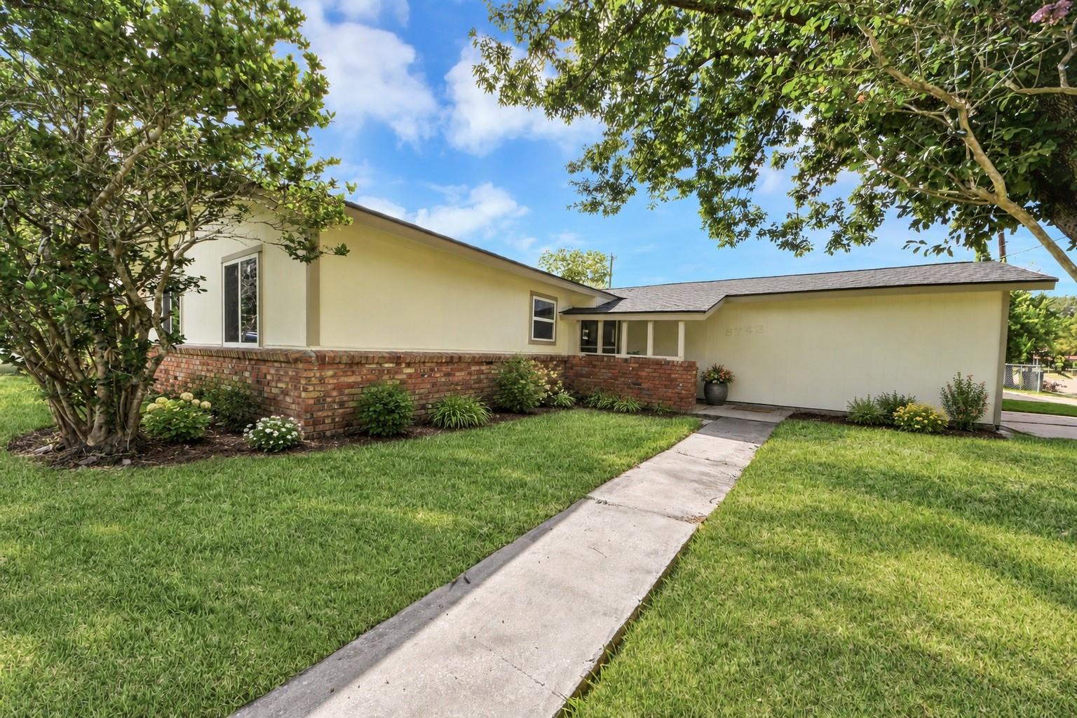 Single-story home with a red-brick front wall, mature trees, and a walkway across the lawn.