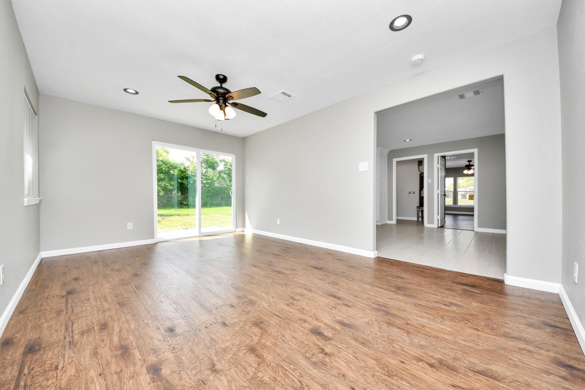 Empty living room with wood flooring, ceiling fan, and sliding glass door to the backyard.