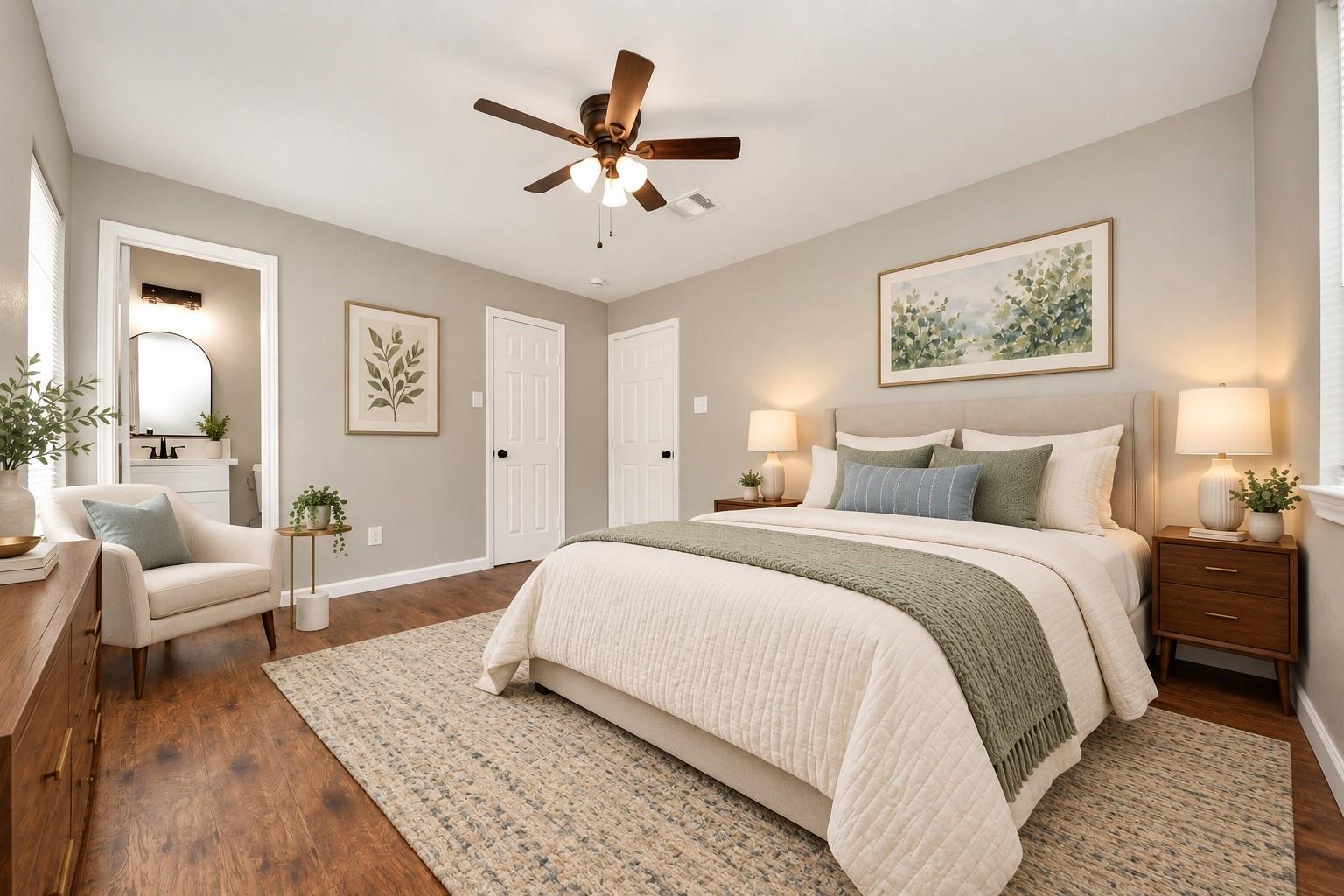 Bedroom with a white bed, sage-green throw, hardwood floors, and an open doorway to the bathroom.