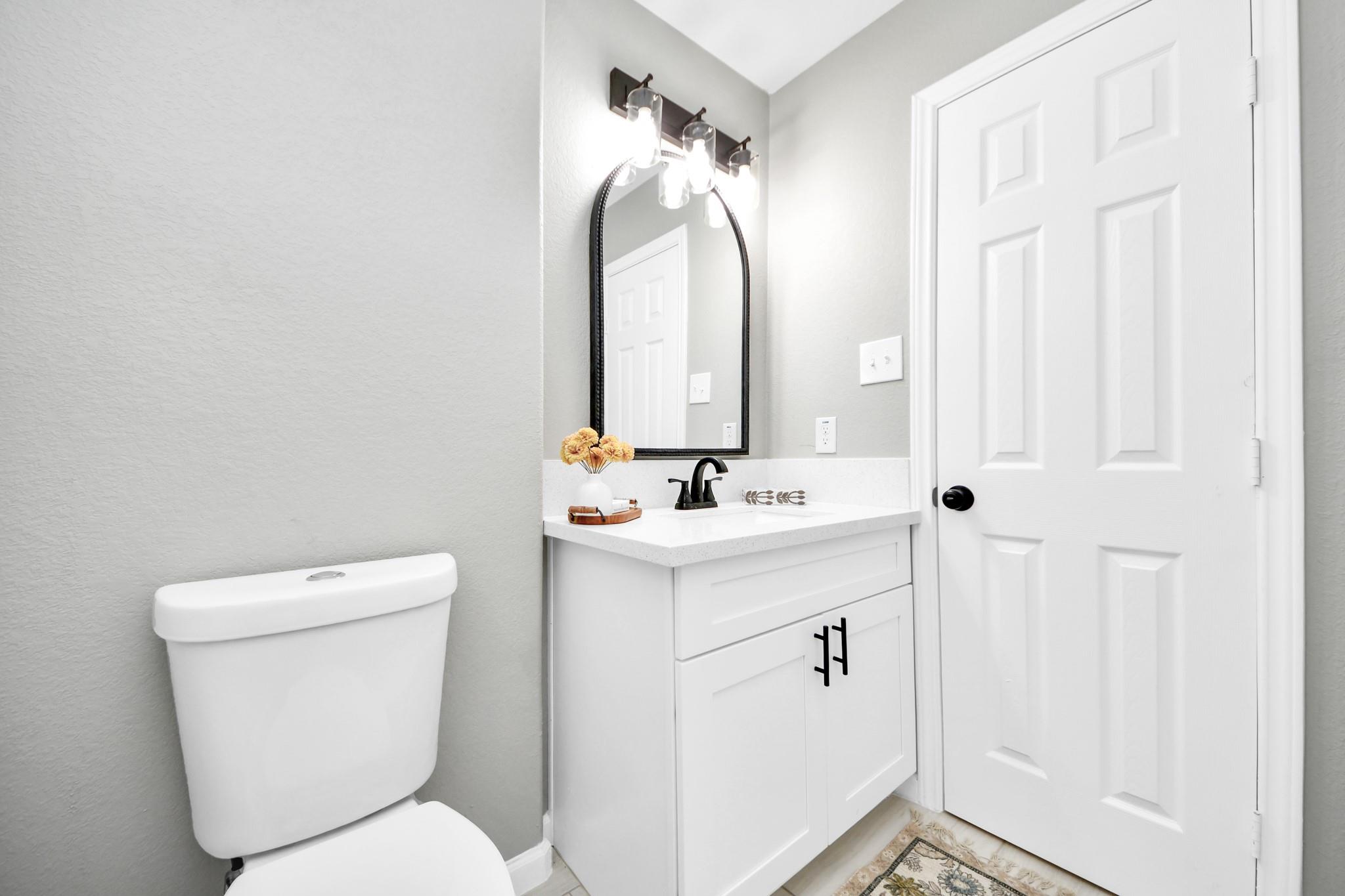 Bathroom with white vanity, black fixtures, arched mirror, and toilet.