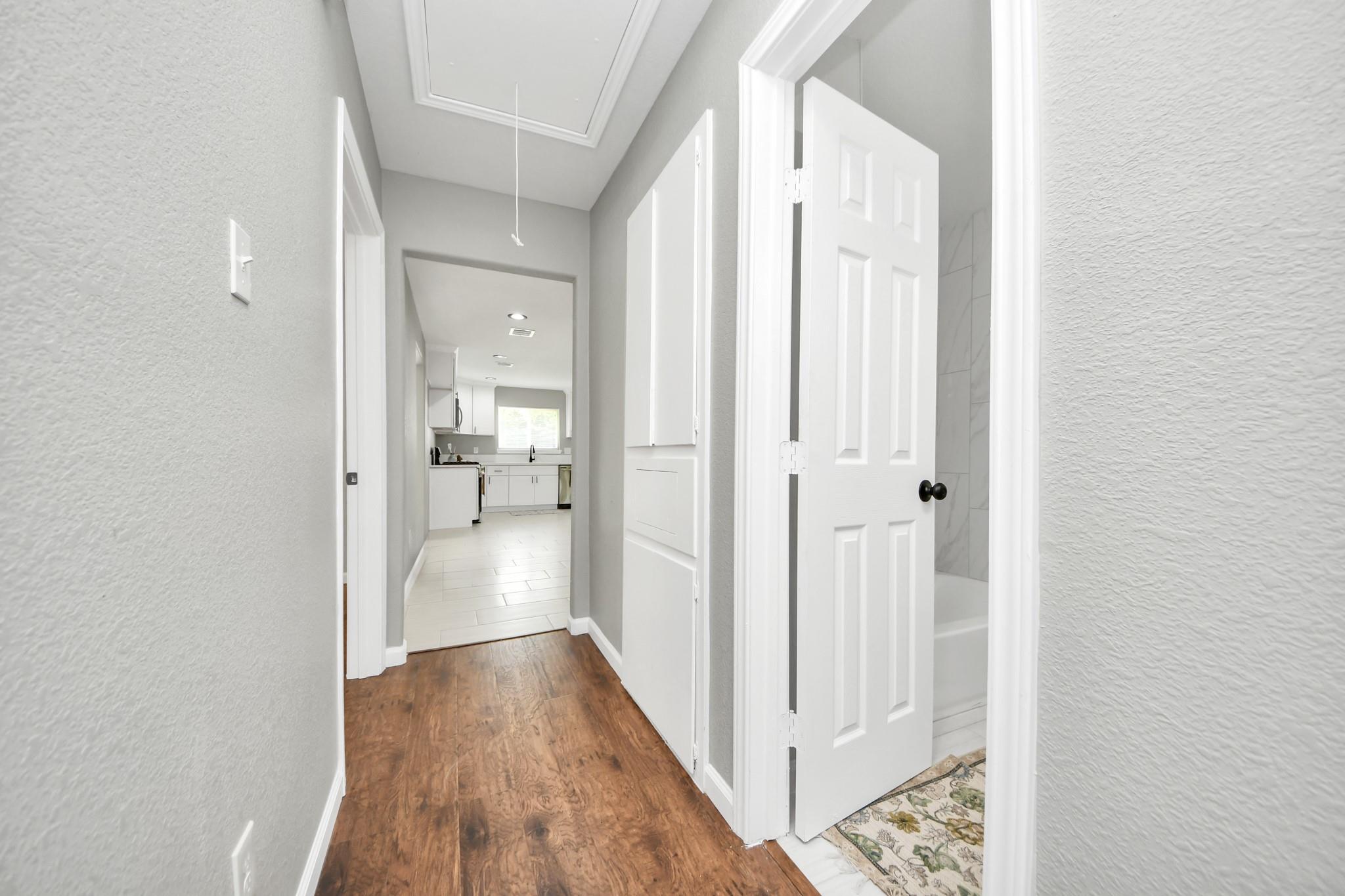 Hallway with wood-look floors, an open bathroom door, and a white kitchen at the end.