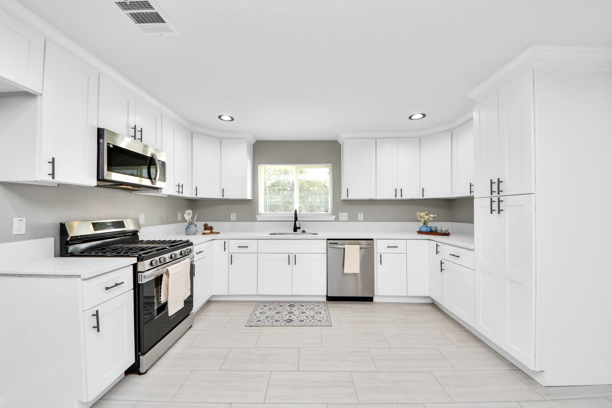 Bright white kitchen with shaker cabinets, stainless steel appliances, and a window above the sink.